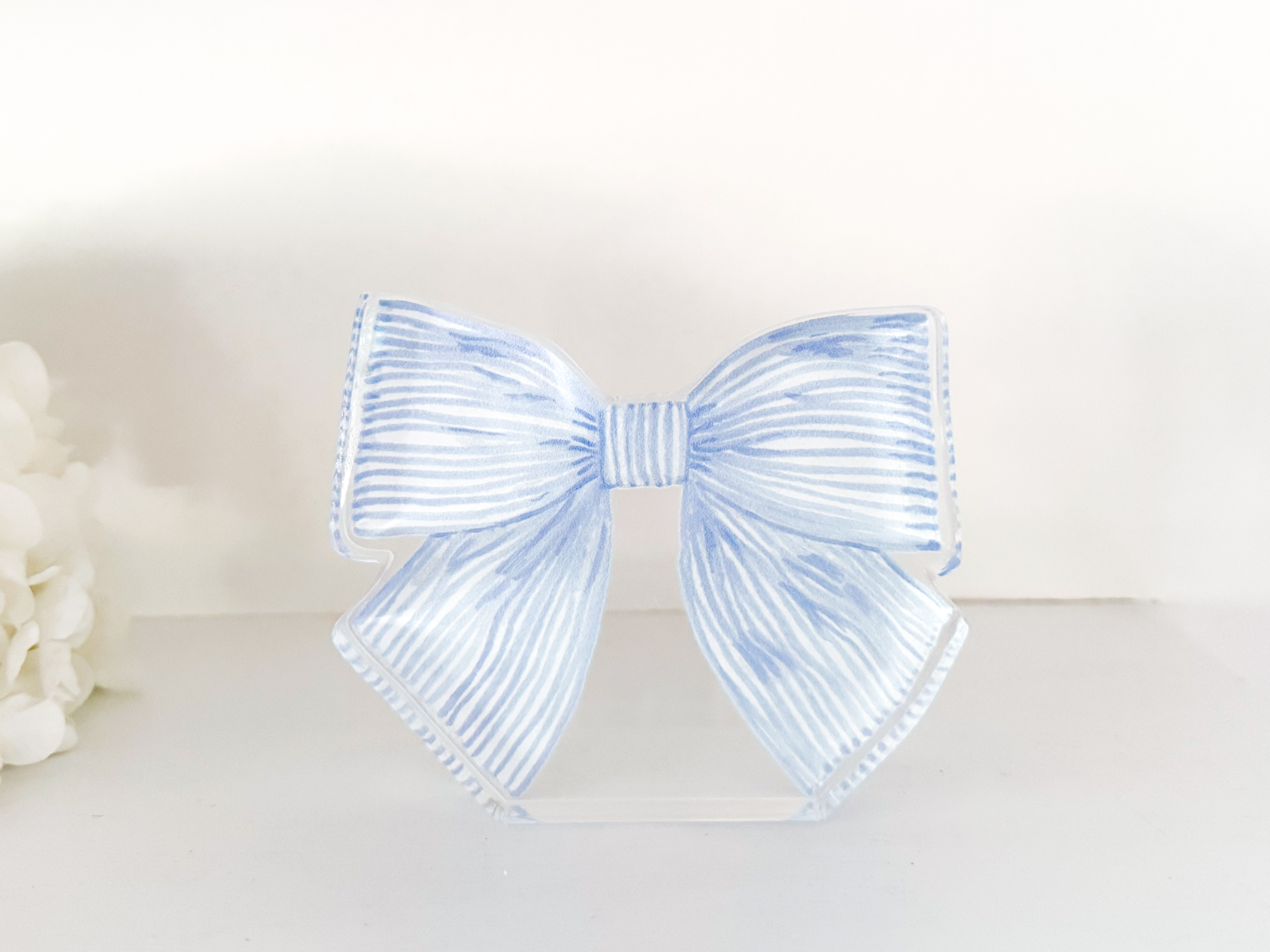 A blue and white striped bow tie is displayed on a white surface, with a white flower visible to the left.