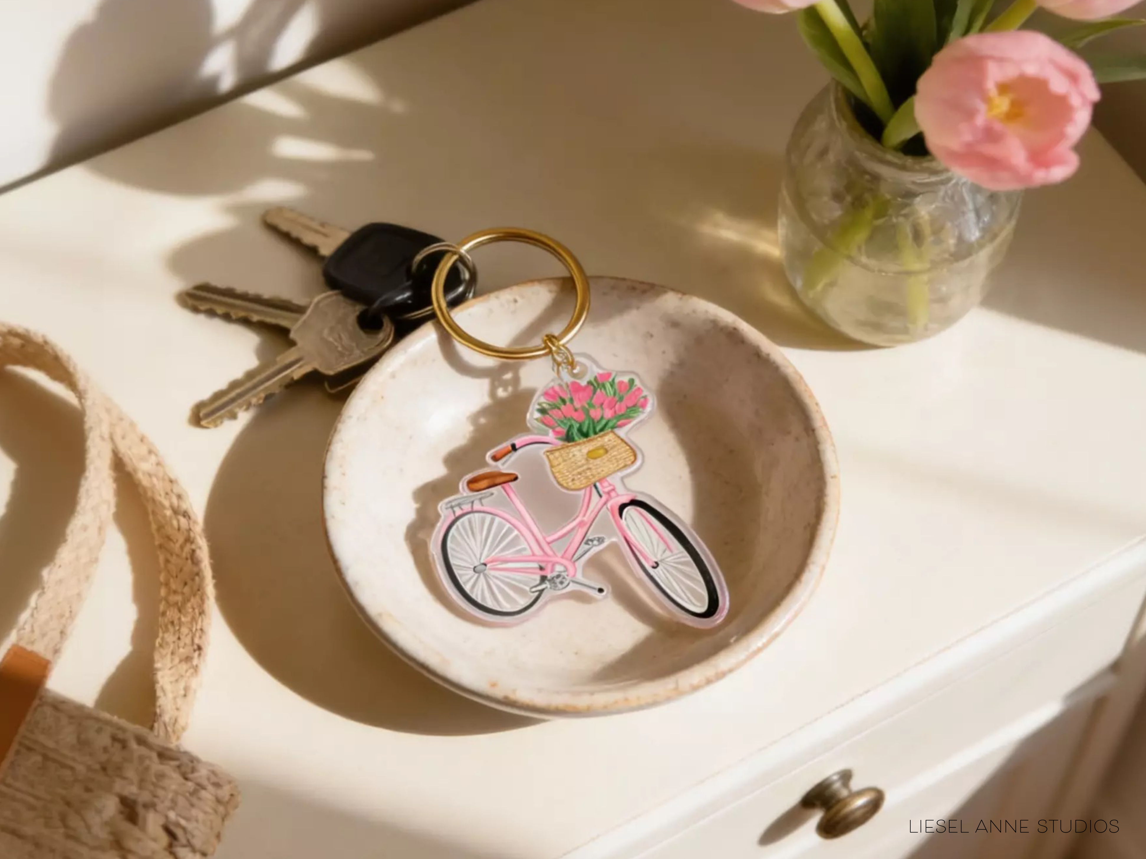 A keychain with a pink bicycle and a vase of pink flowers on a white surface.