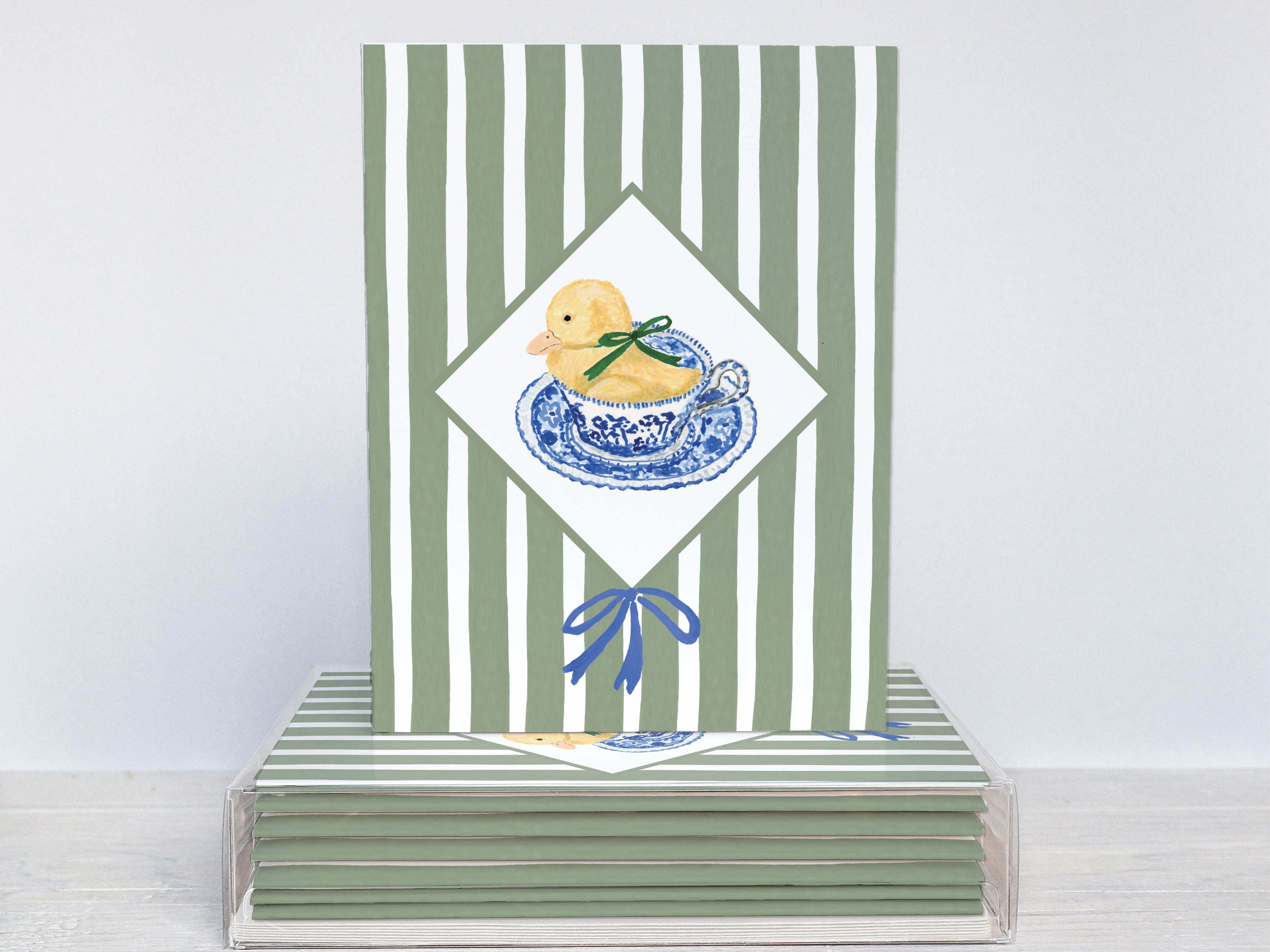 A green and white striped card with a blue and white teacup and yellow duck on it, placed on a stack of similar cards.