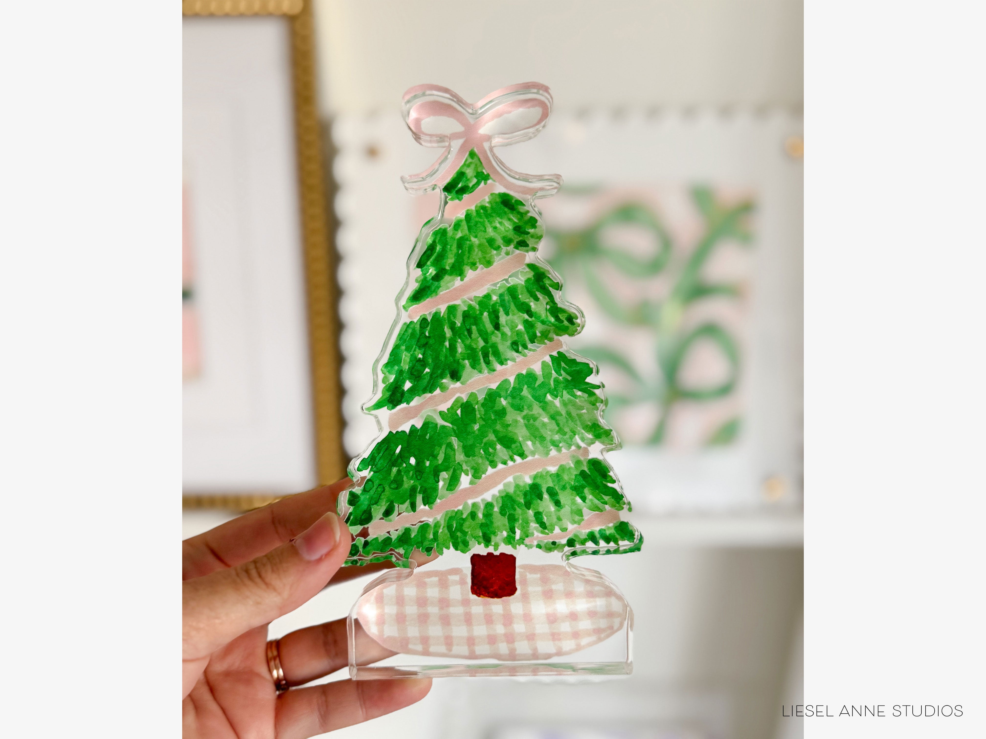 A hand holding a clear glass Christmas tree ornament with a pink ribbon bow.