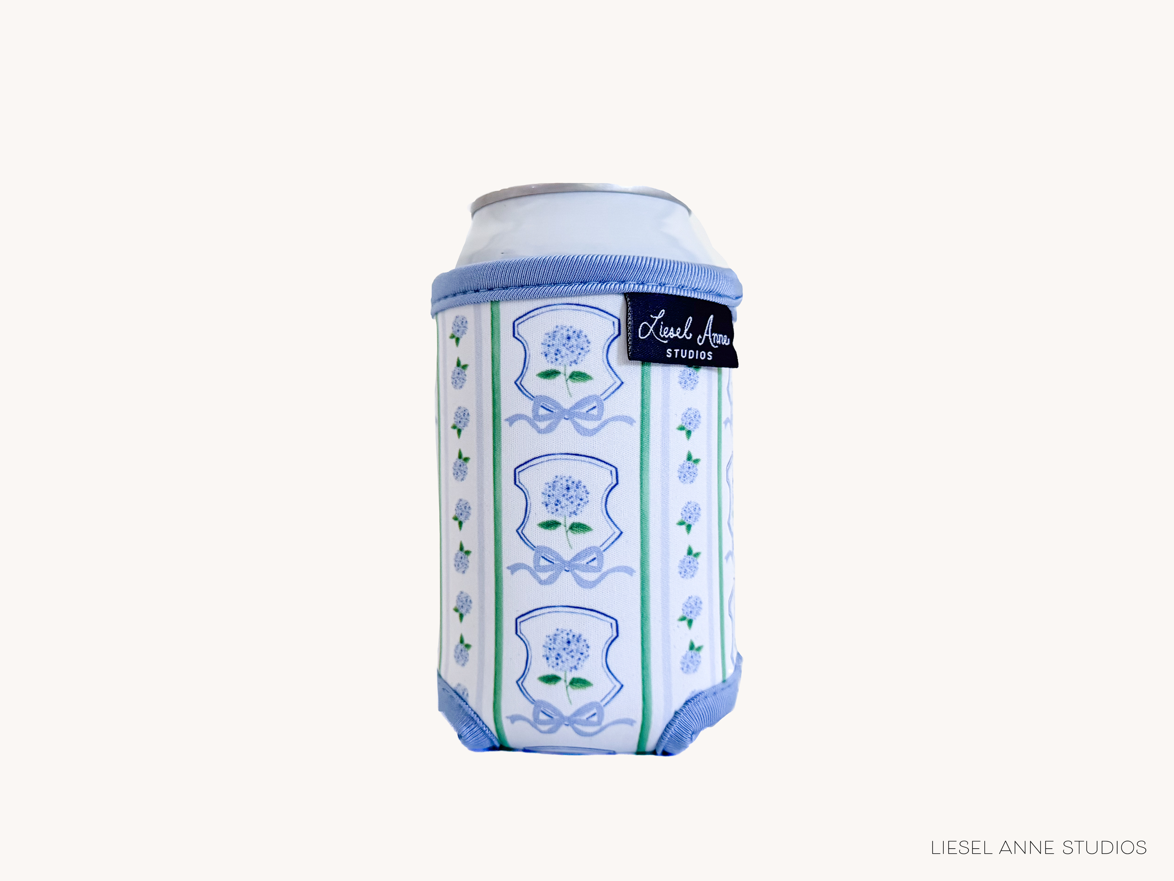 A blue and white can holder with a floral pattern and a label that says "Liesel Anne Studios".