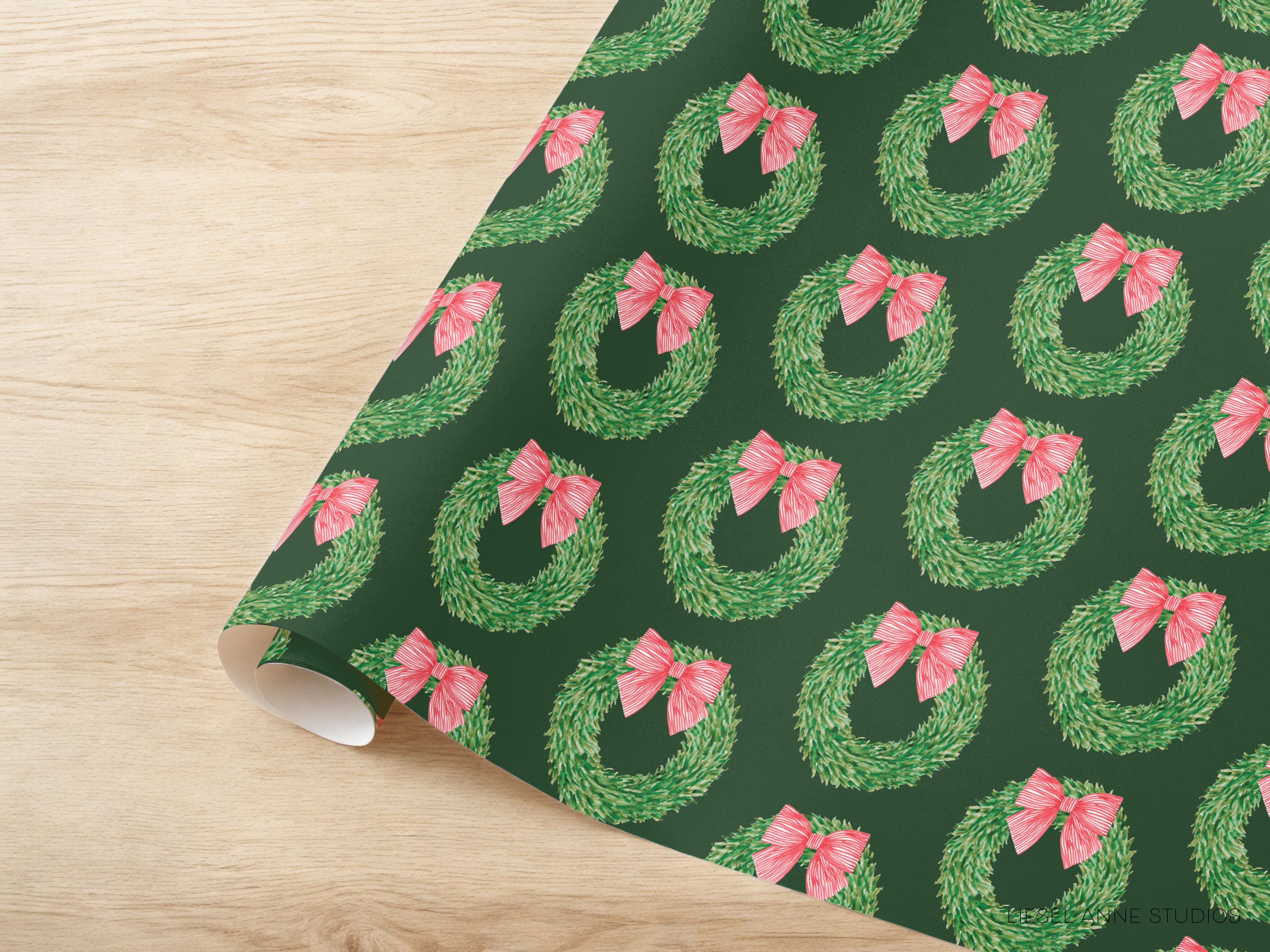 a roll of wrapping paper with a repeating pattern of green Christmas wreaths with pink bows on a dark green background.