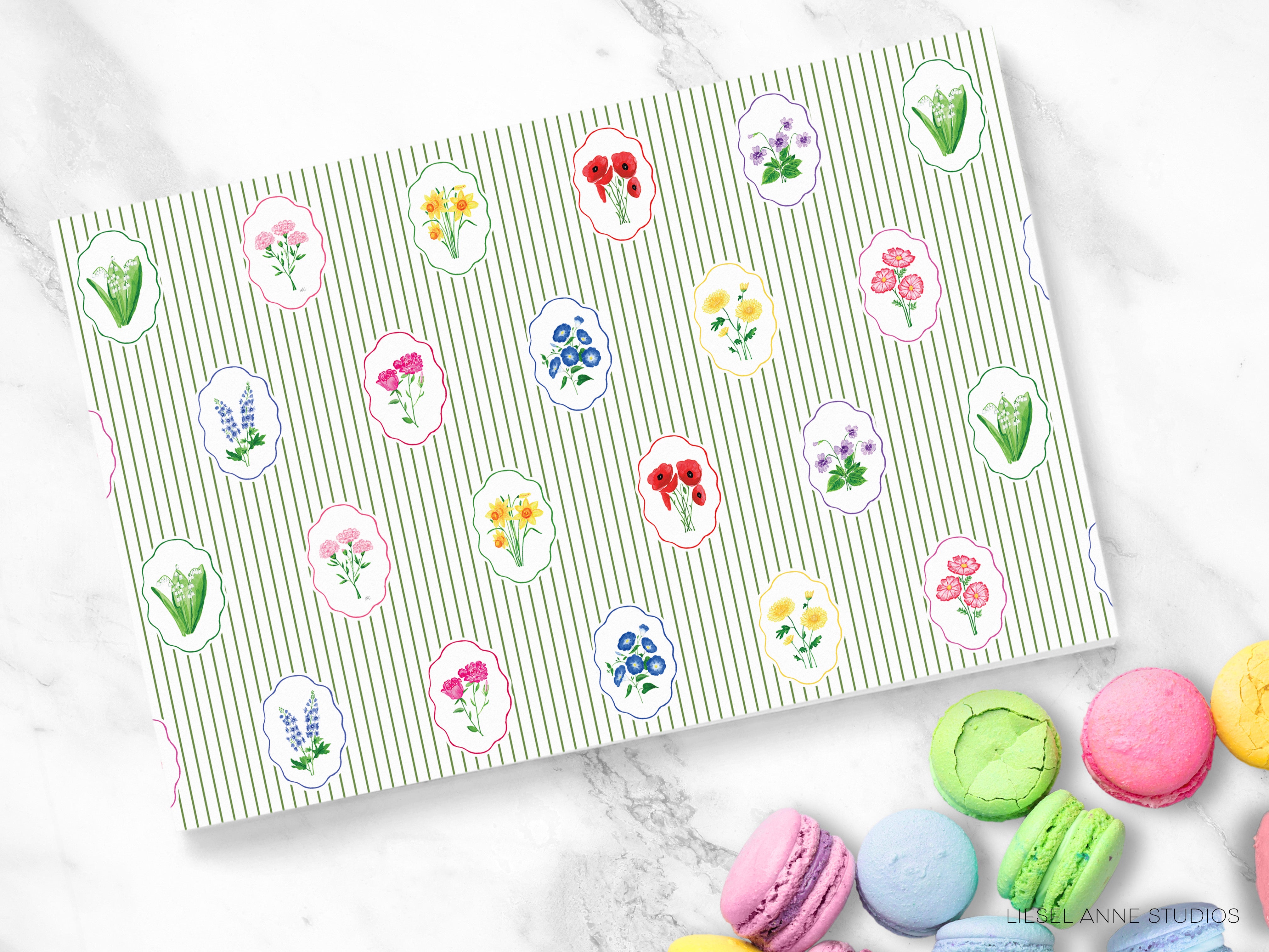 a collection of colorful macarons arranged on a marble surface, with a pattern of flower motifs on a green and white striped background.