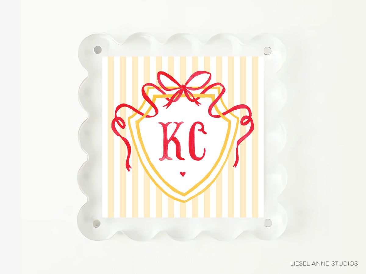 A square image with a yellow and white striped background, featuring a red ribbon and a shield-shaped design with the initials "KC" prominently displayed.