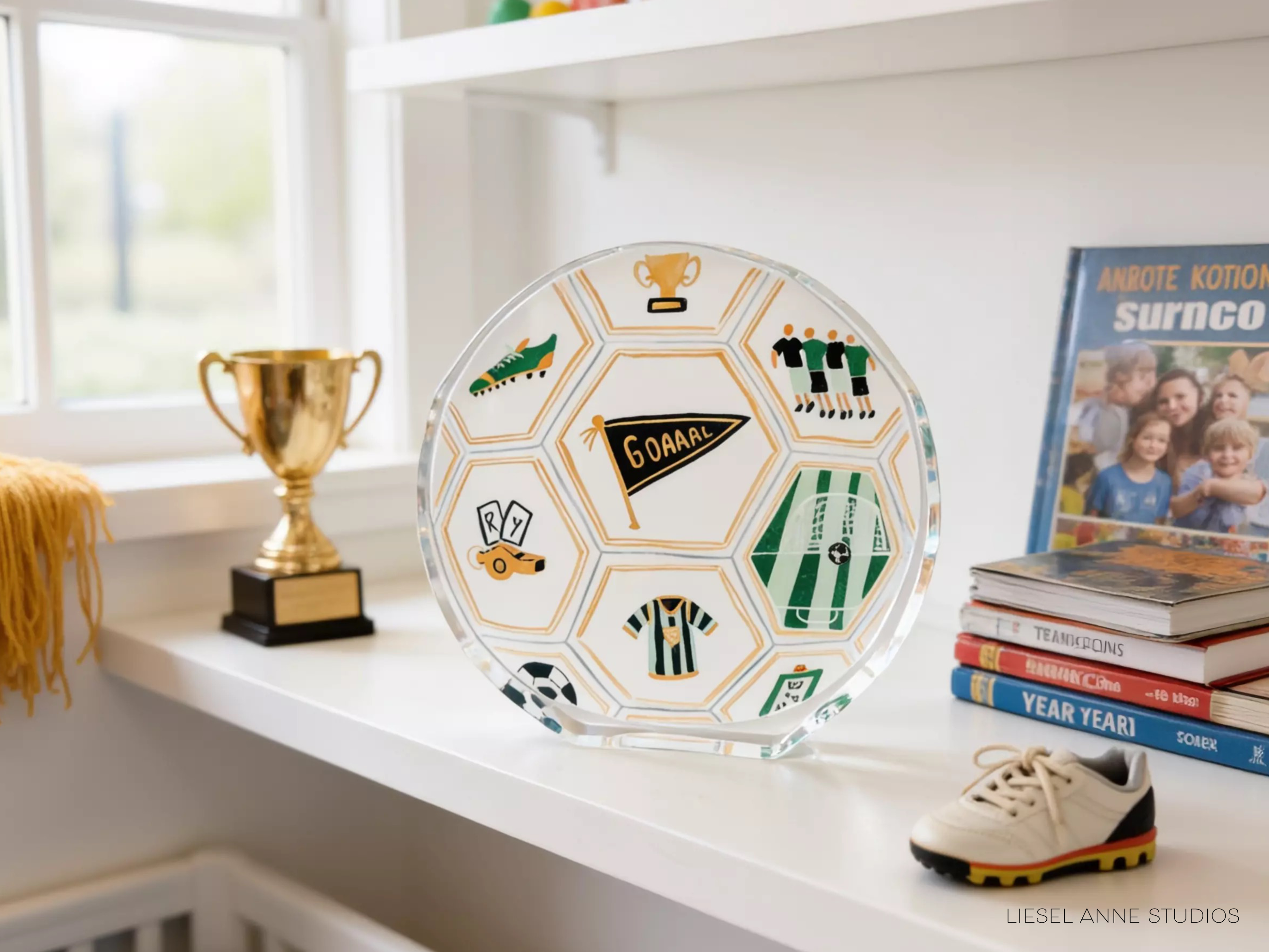 a soccer-themed trophy, a trophy cup, a soccer ball, a book, and a pair of shoes on a shelf.