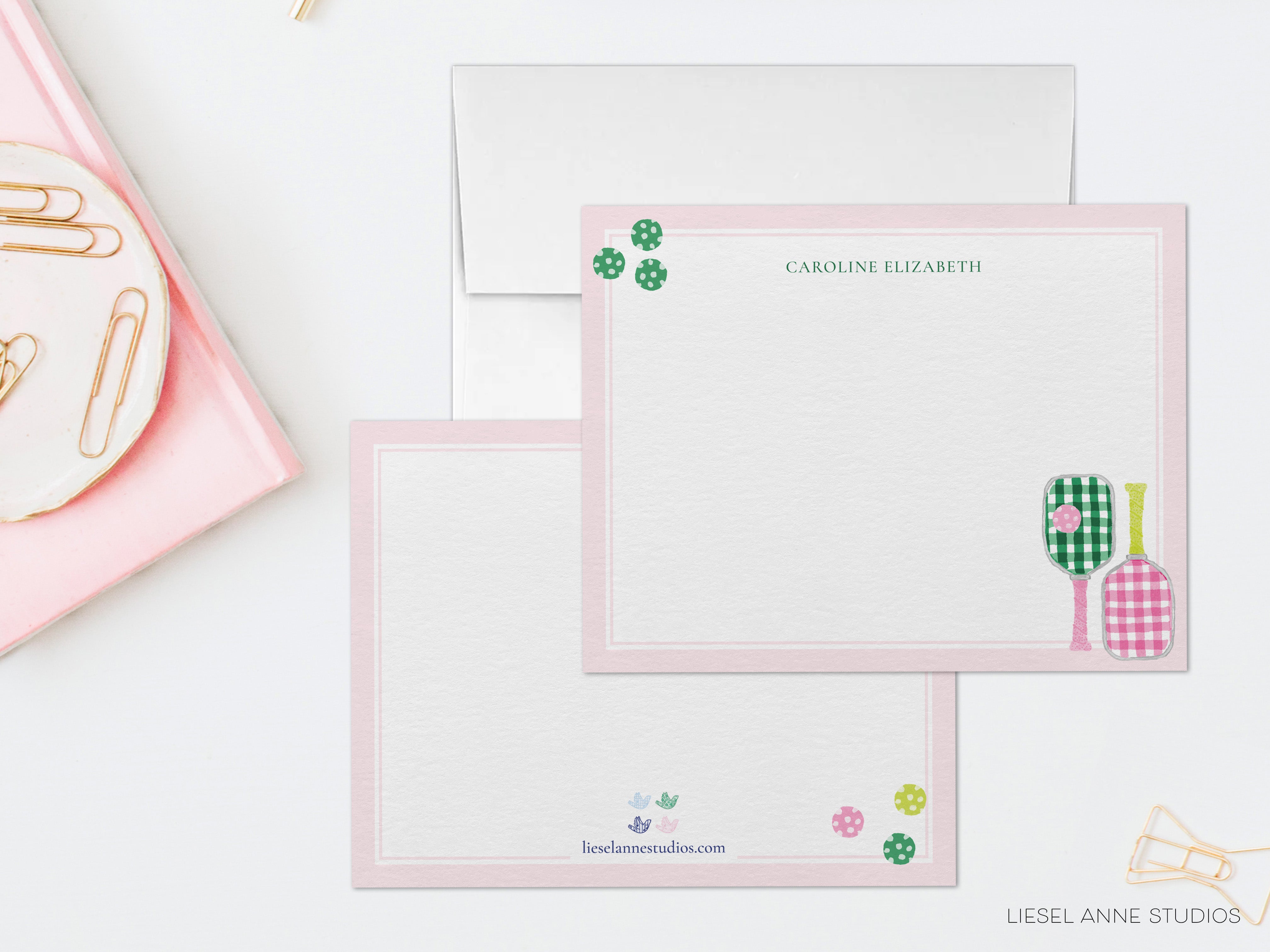 a pink envelope with a blank card inside, placed on a white surface. There are also some office supplies, such as a stapler and a pair of scissors, visible in the scene.