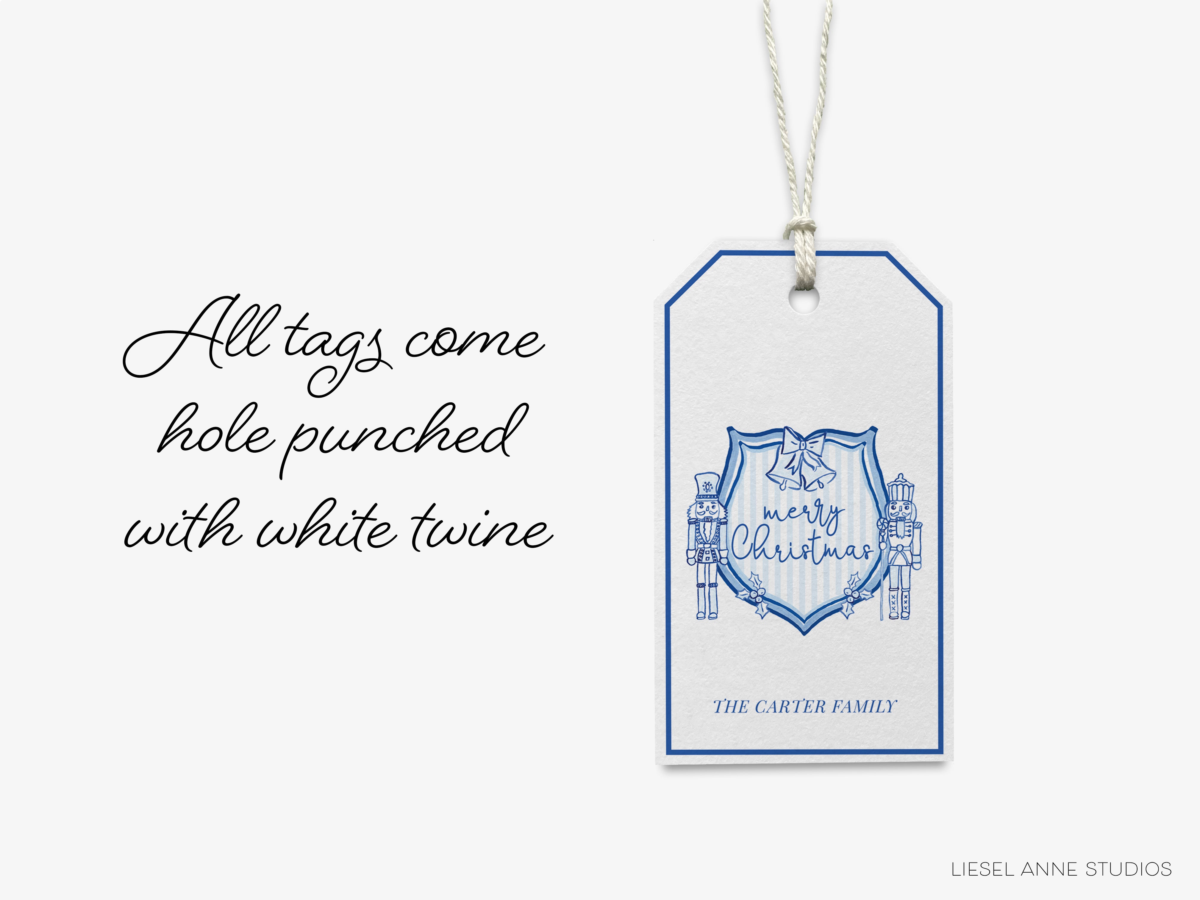 A white tag with a blue design hanging from a string, featuring the text "All tags come hole punched with white twine" and an illustration of a nutcracker with bells.
