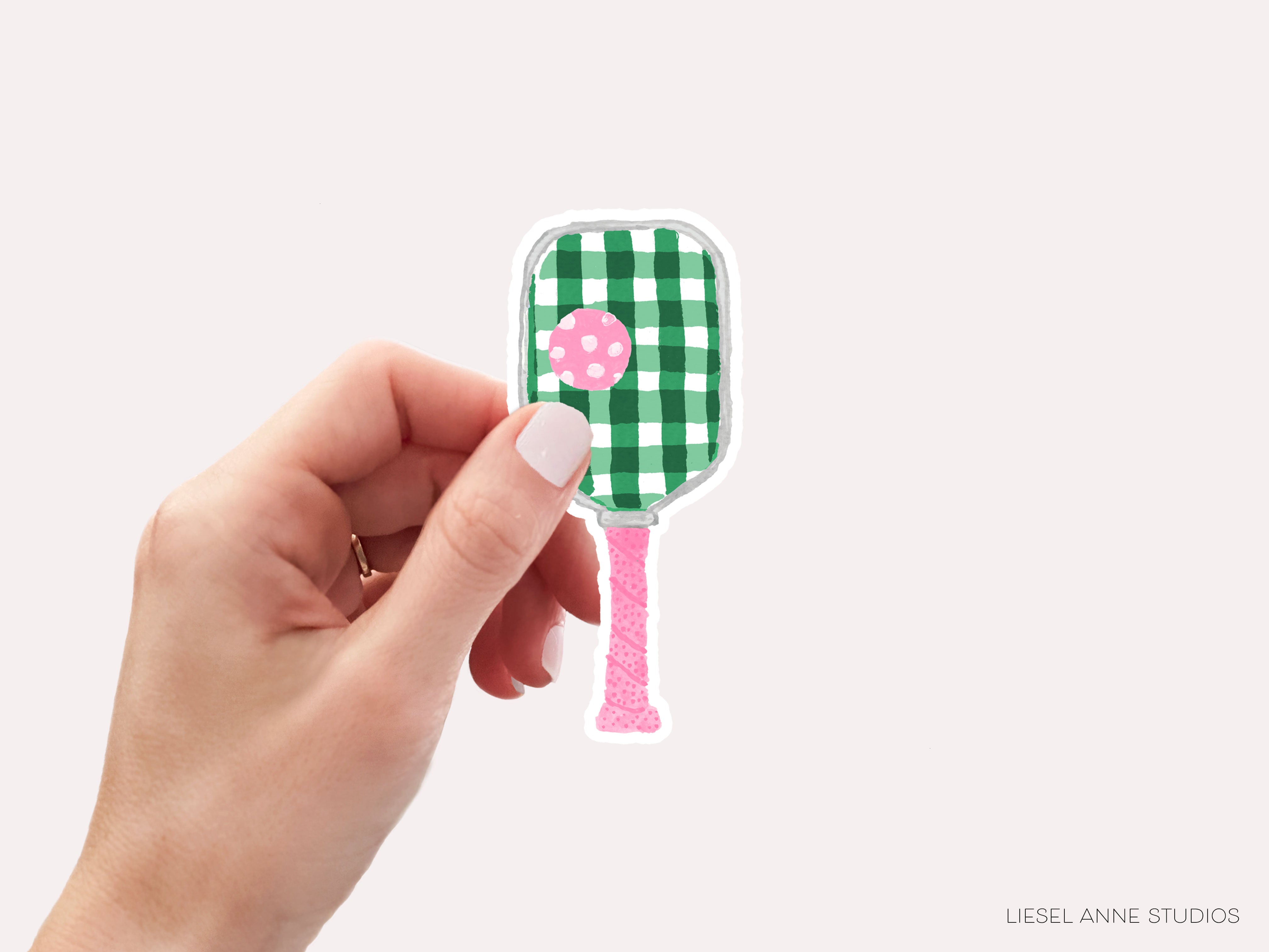 A hand holding a green and white paddle with a pink polka dot on it.