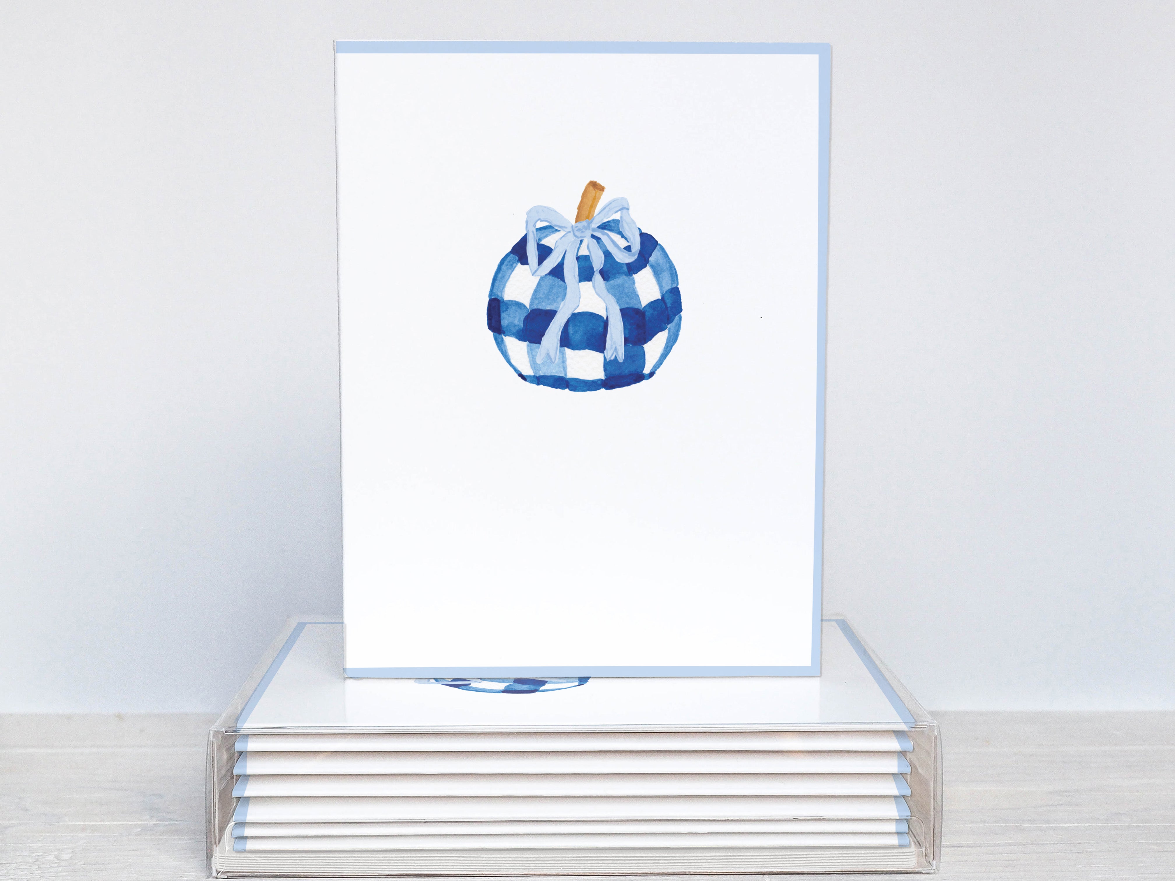 A white card with a blue and white checkered pumpkin design on it, placed on top of a stack of similar cards.