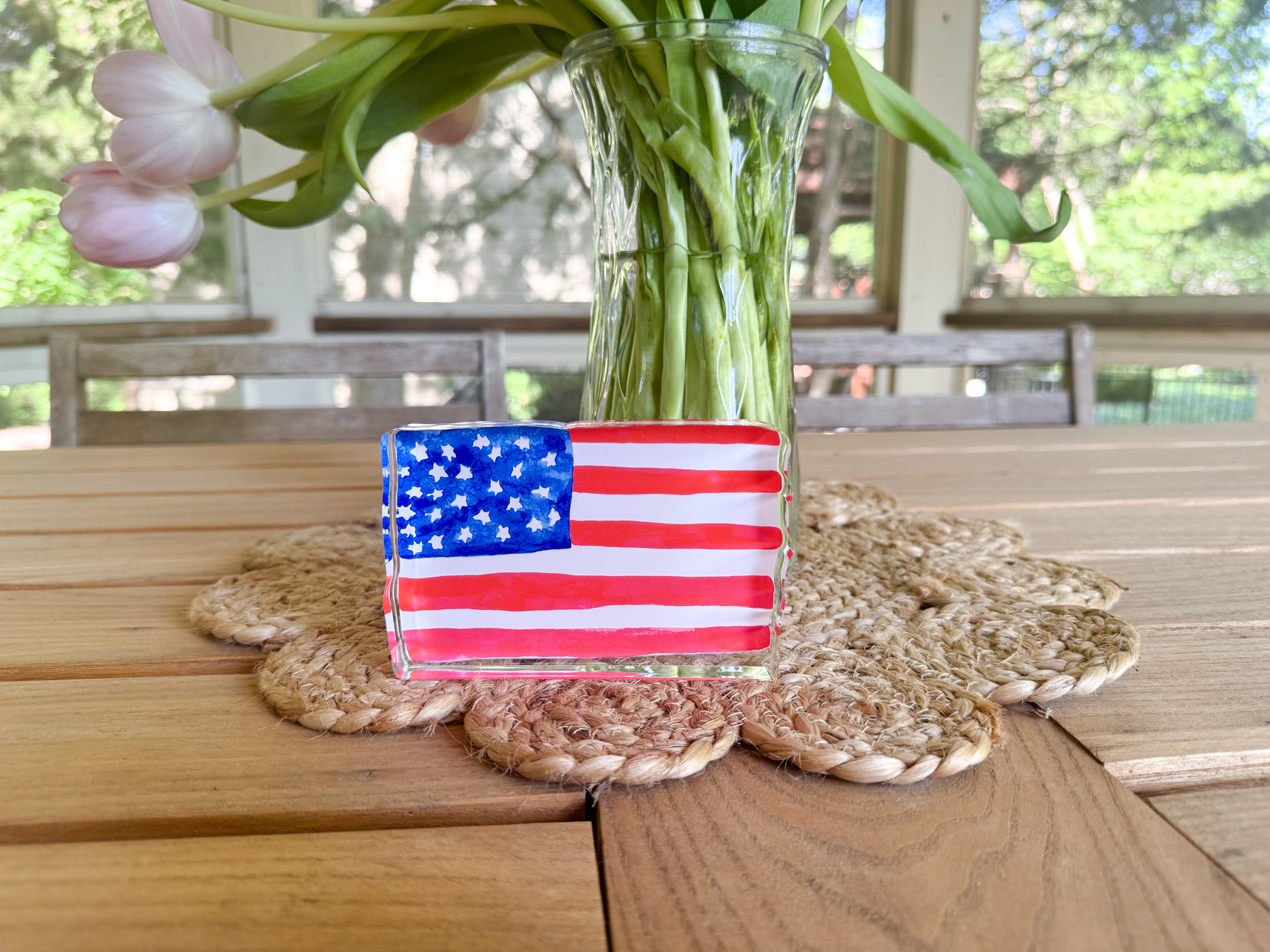a wooden table with a vase of green leaves and a glass container holding a painted American flag.
