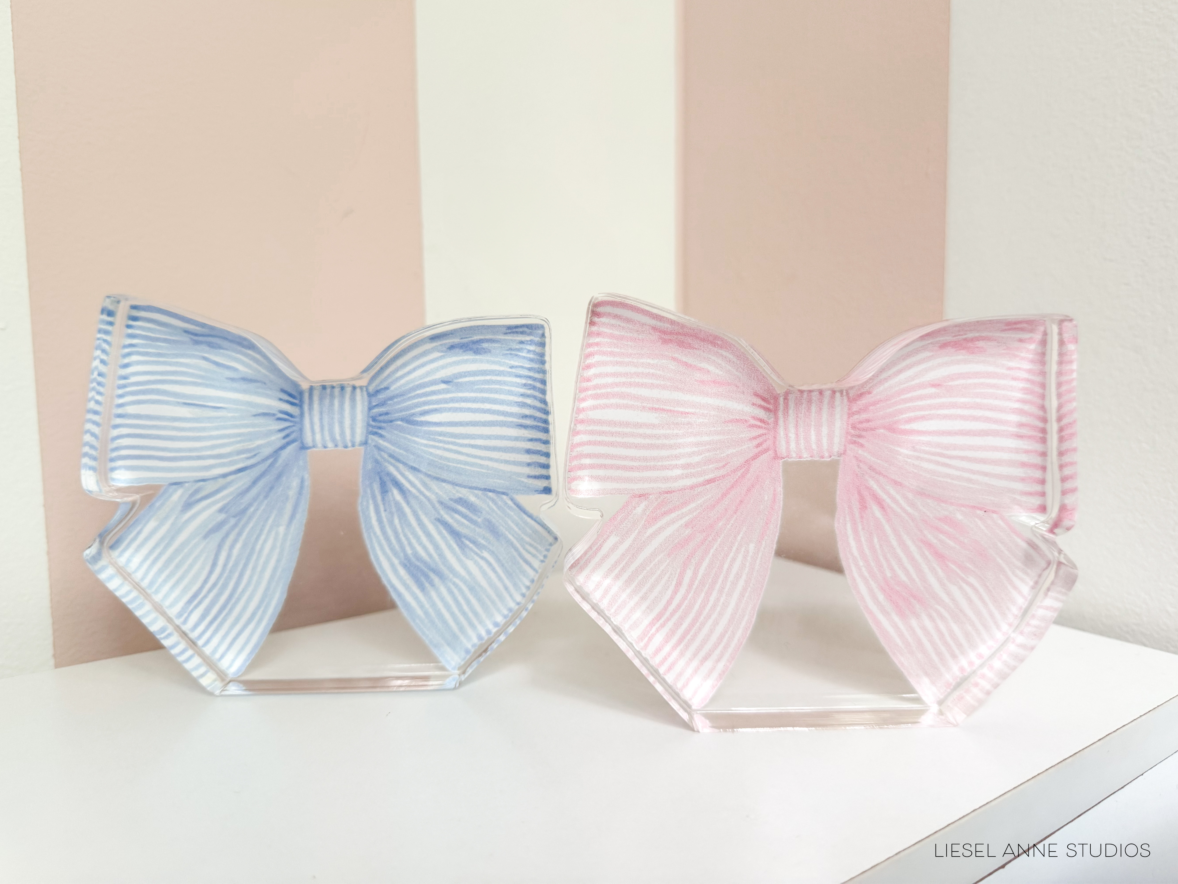 Two decorative bows in different colors - blue and pink - are displayed on a white surface.