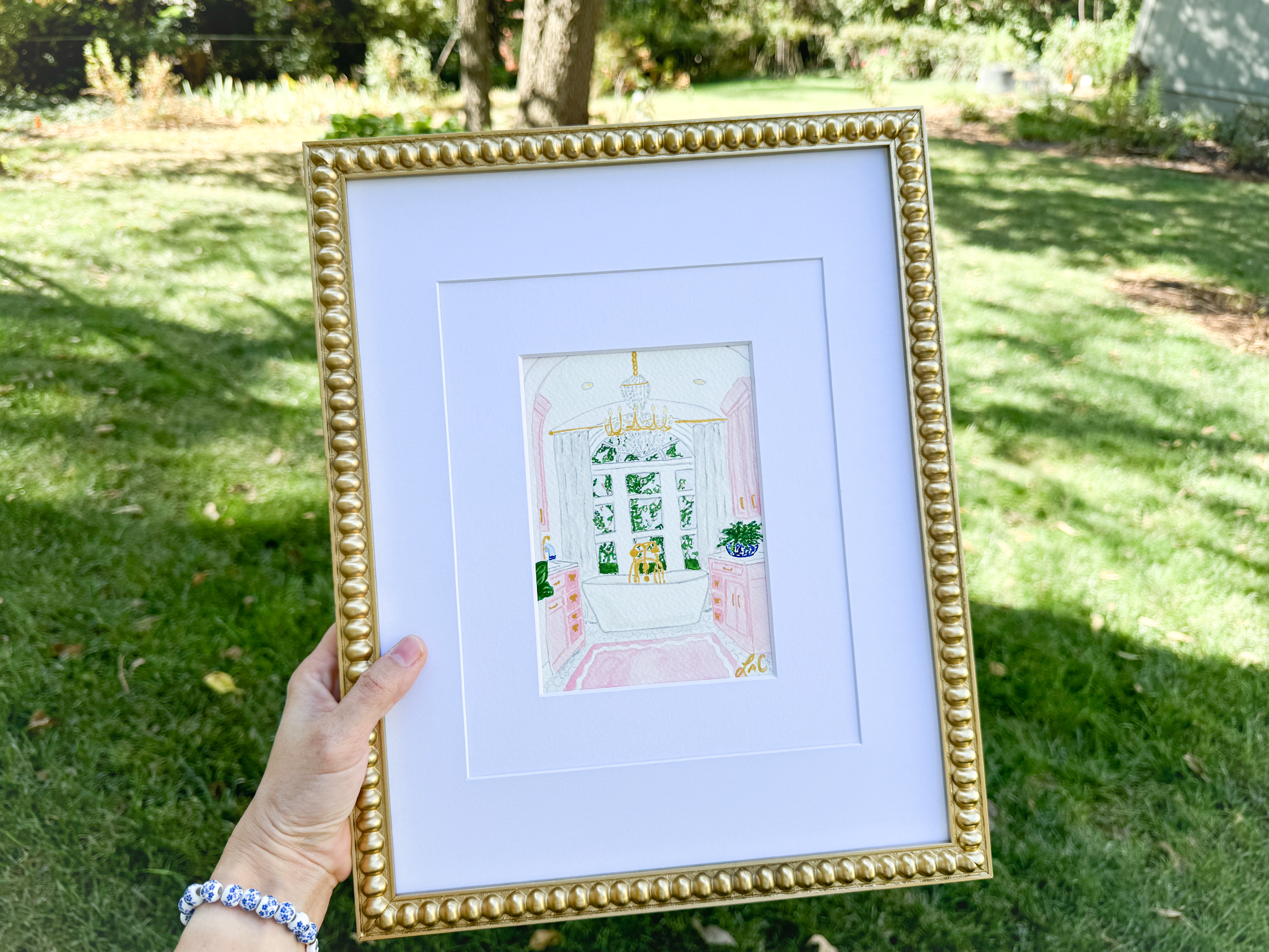 A hand holding a framed painting of a white door with a pink interior, set against a green background.