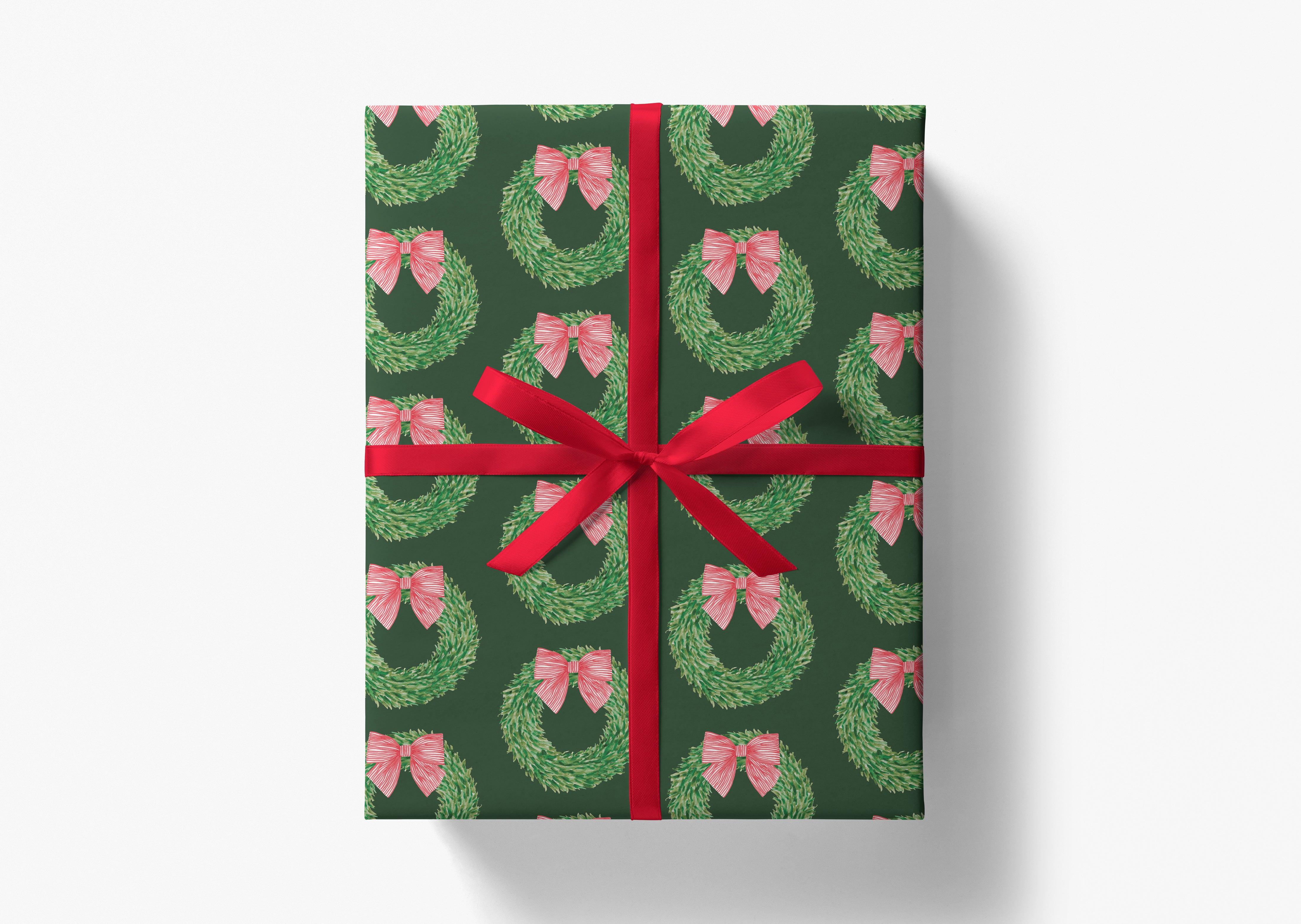 A gift box wrapped in a pattern of green wreaths with red bows tied around them, tied with a red ribbon.