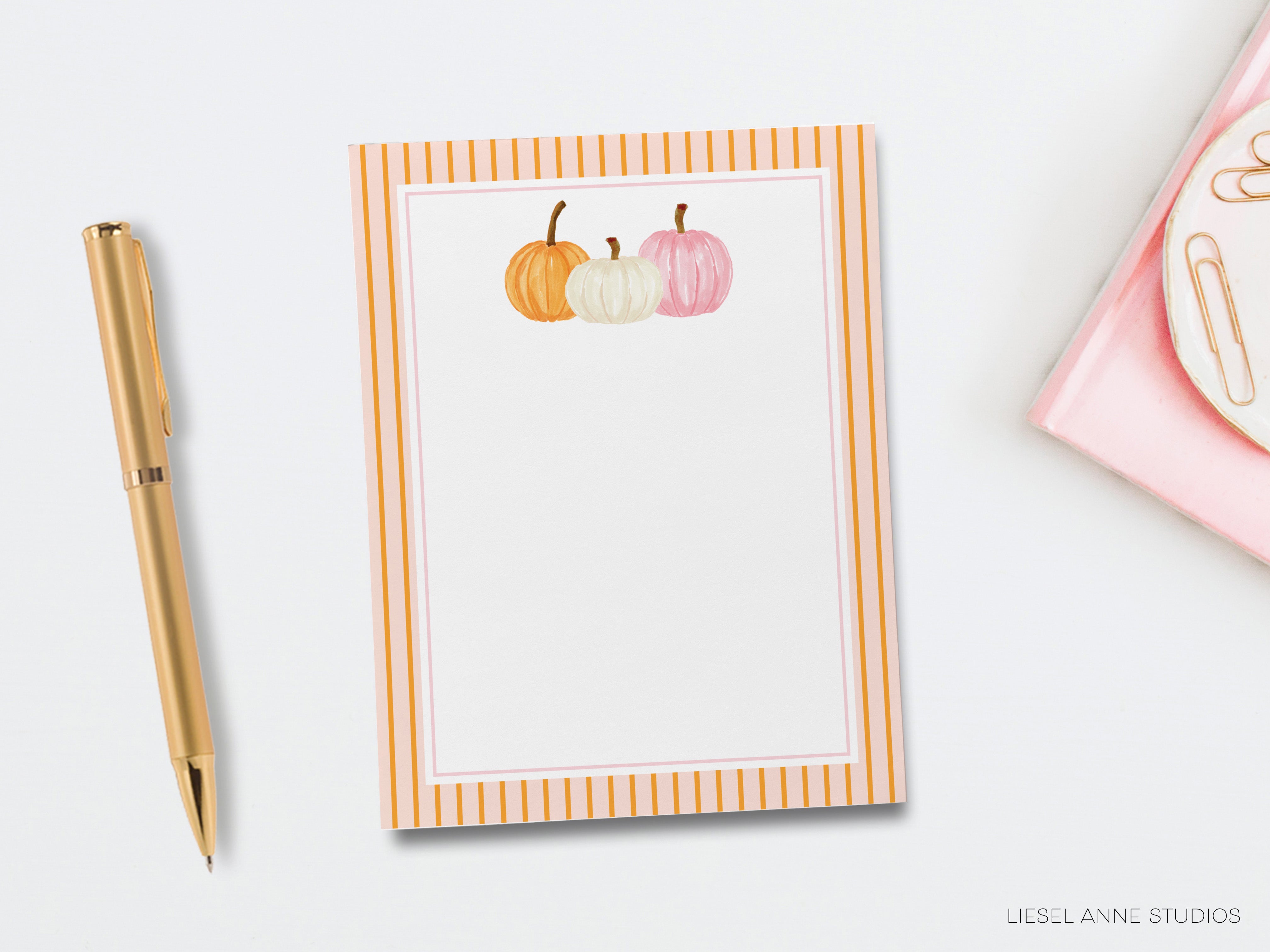 a blank card with a decorative border, a gold pen, and a pink object, all placed on a white background.