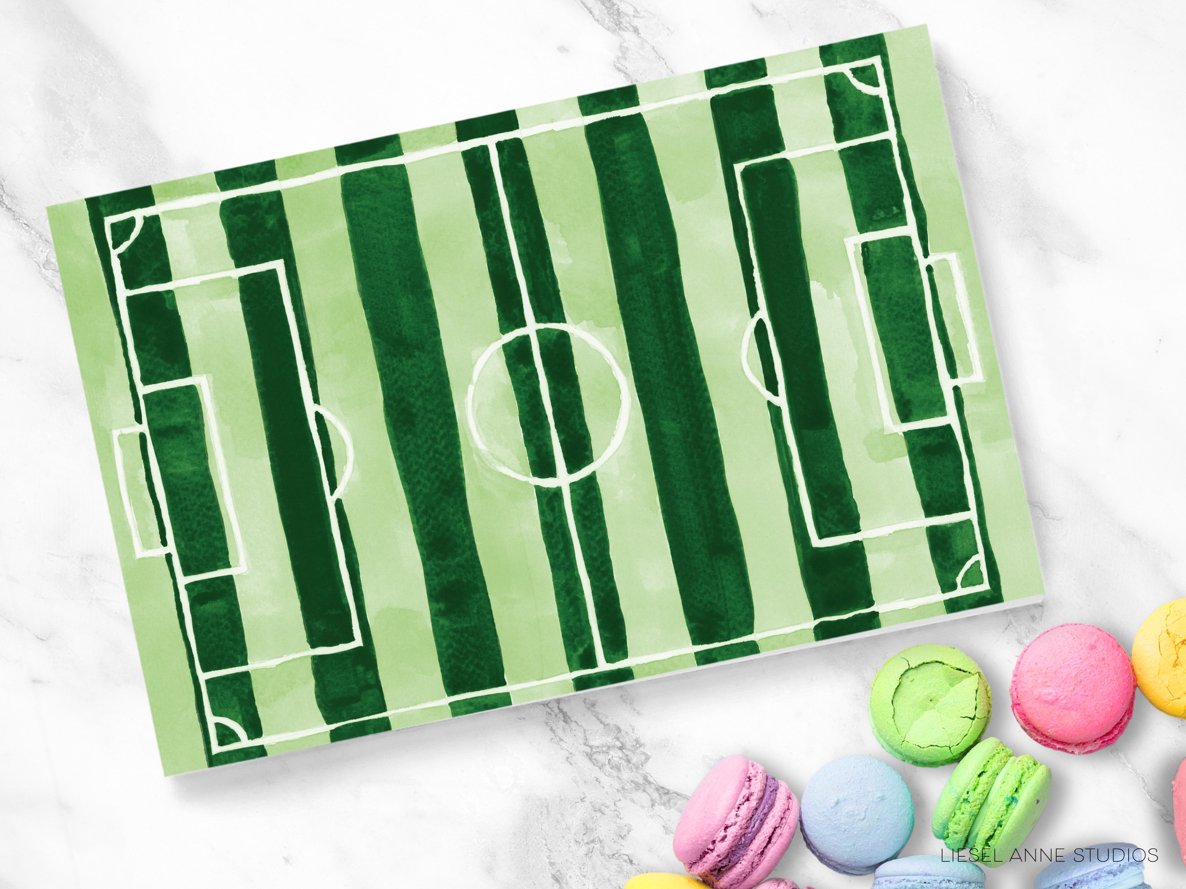 a green and white striped soccer field with a round center, surrounded by an assortment of colorful macarons on a marble surface.
