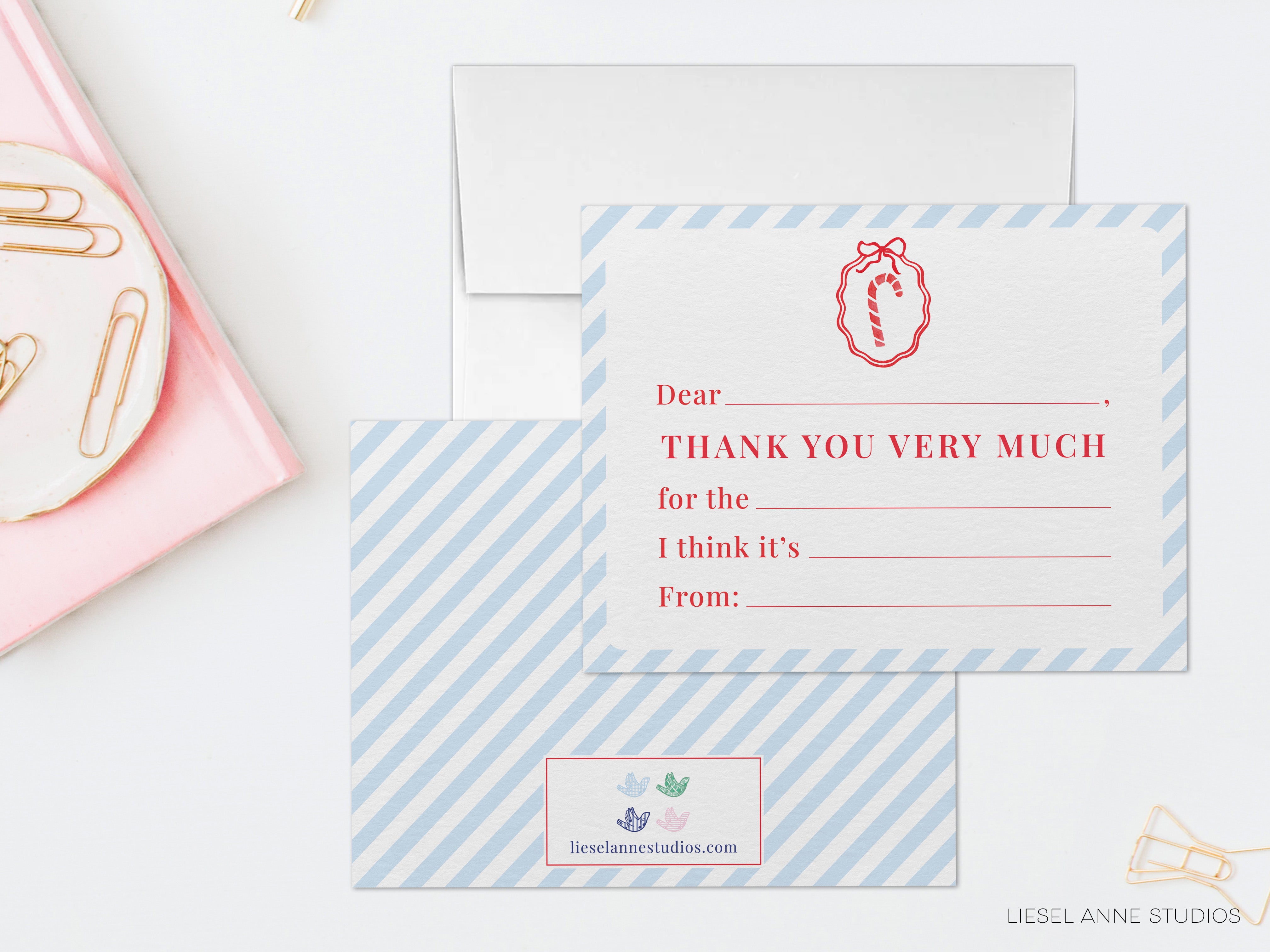 a white card with a blue stripe and a red bow, along with a blank card, a pink plate with a white plate, and some gold clips.