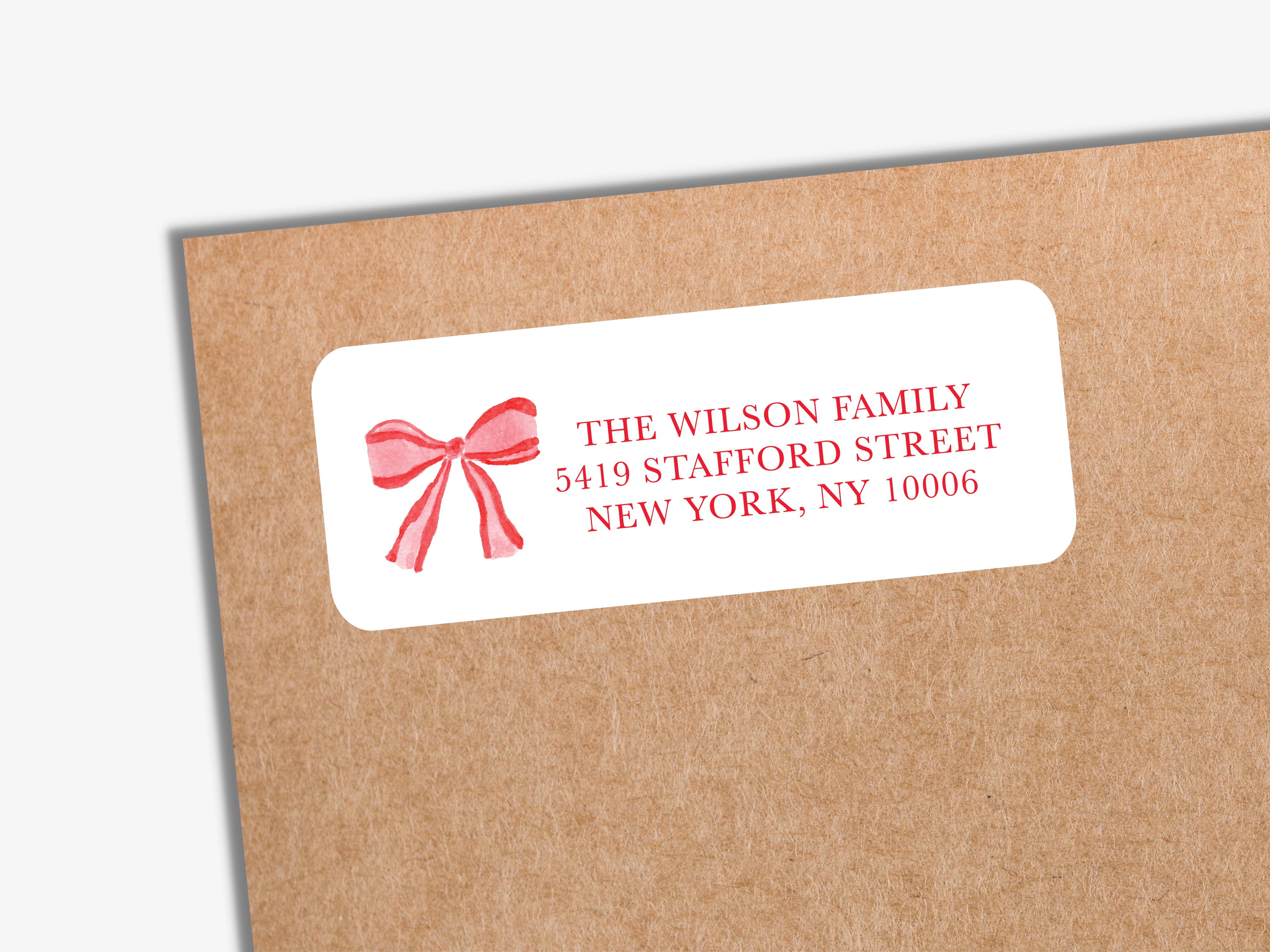 a white envelope label with a red bow on it, placed on a brown envelope.