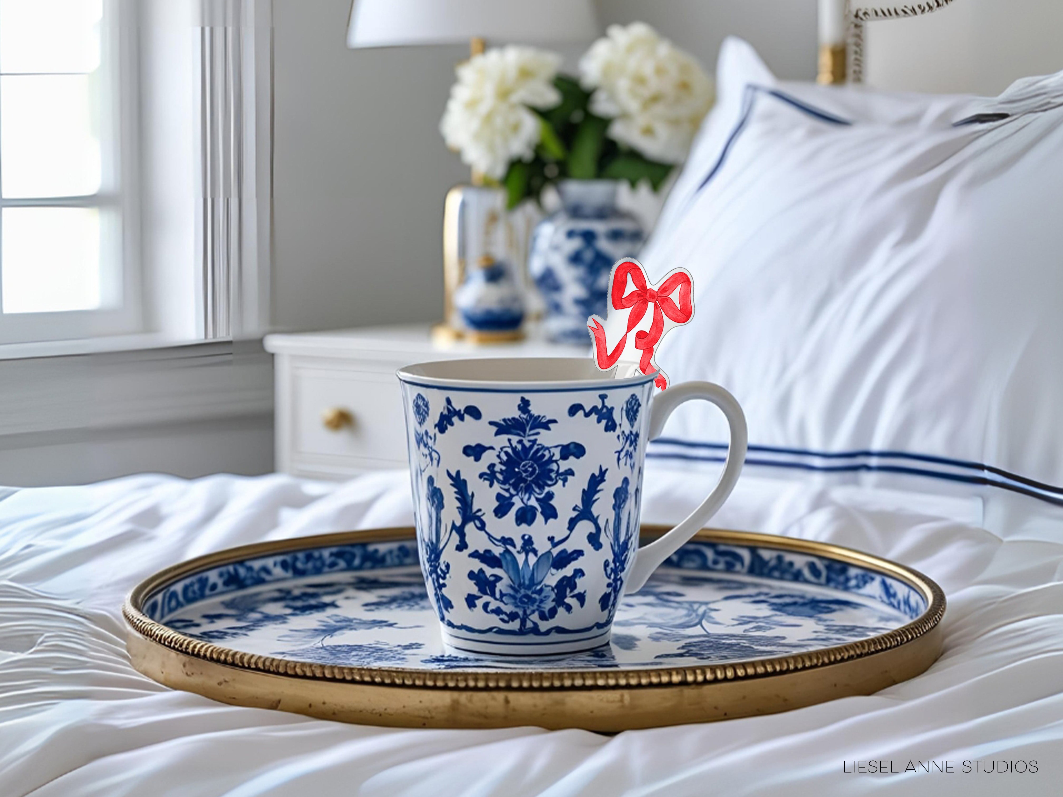 A blue and white patterned mug with a red bow on a tray, placed on a bed with white sheets and a white pillow.