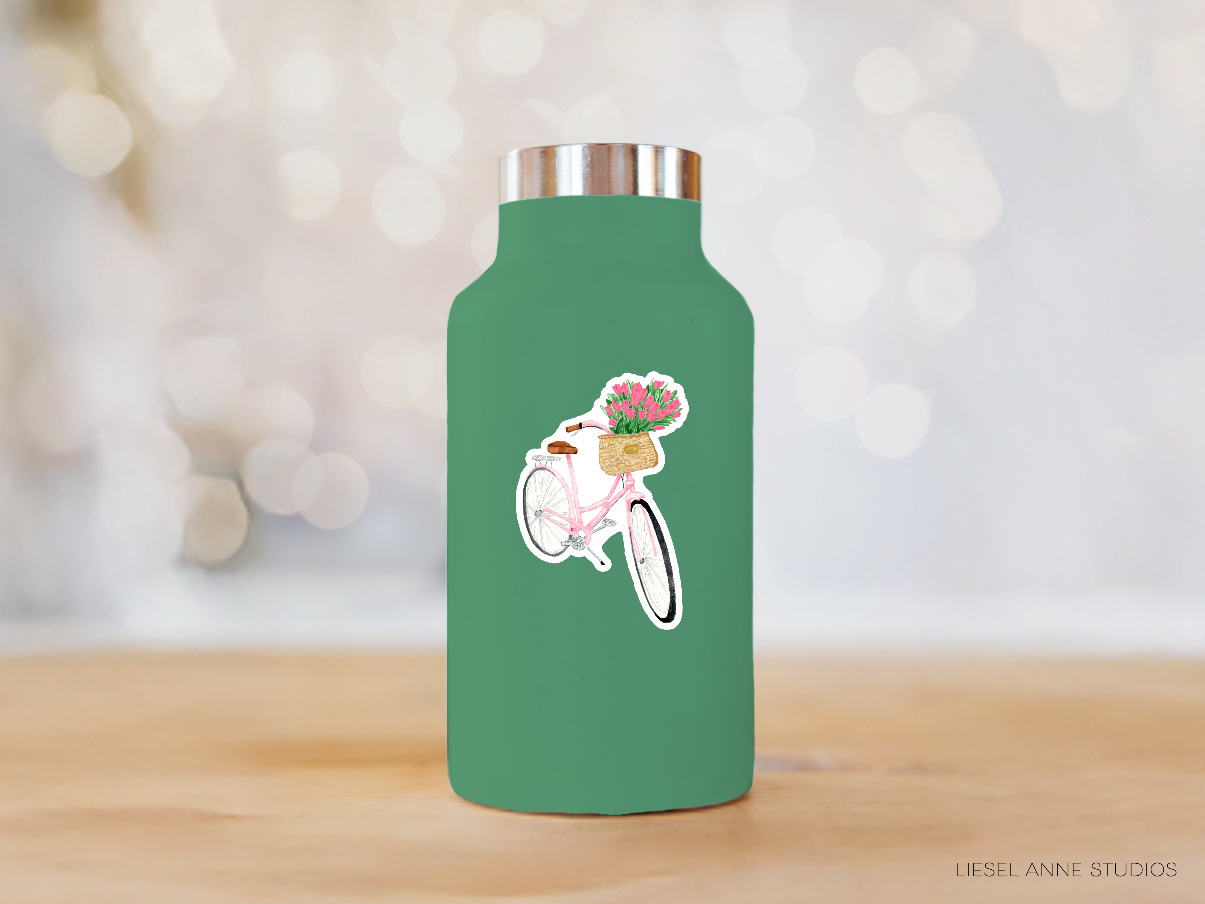 A green water bottle with a sticker of a bicycle and flowers on it, placed on a wooden surface.