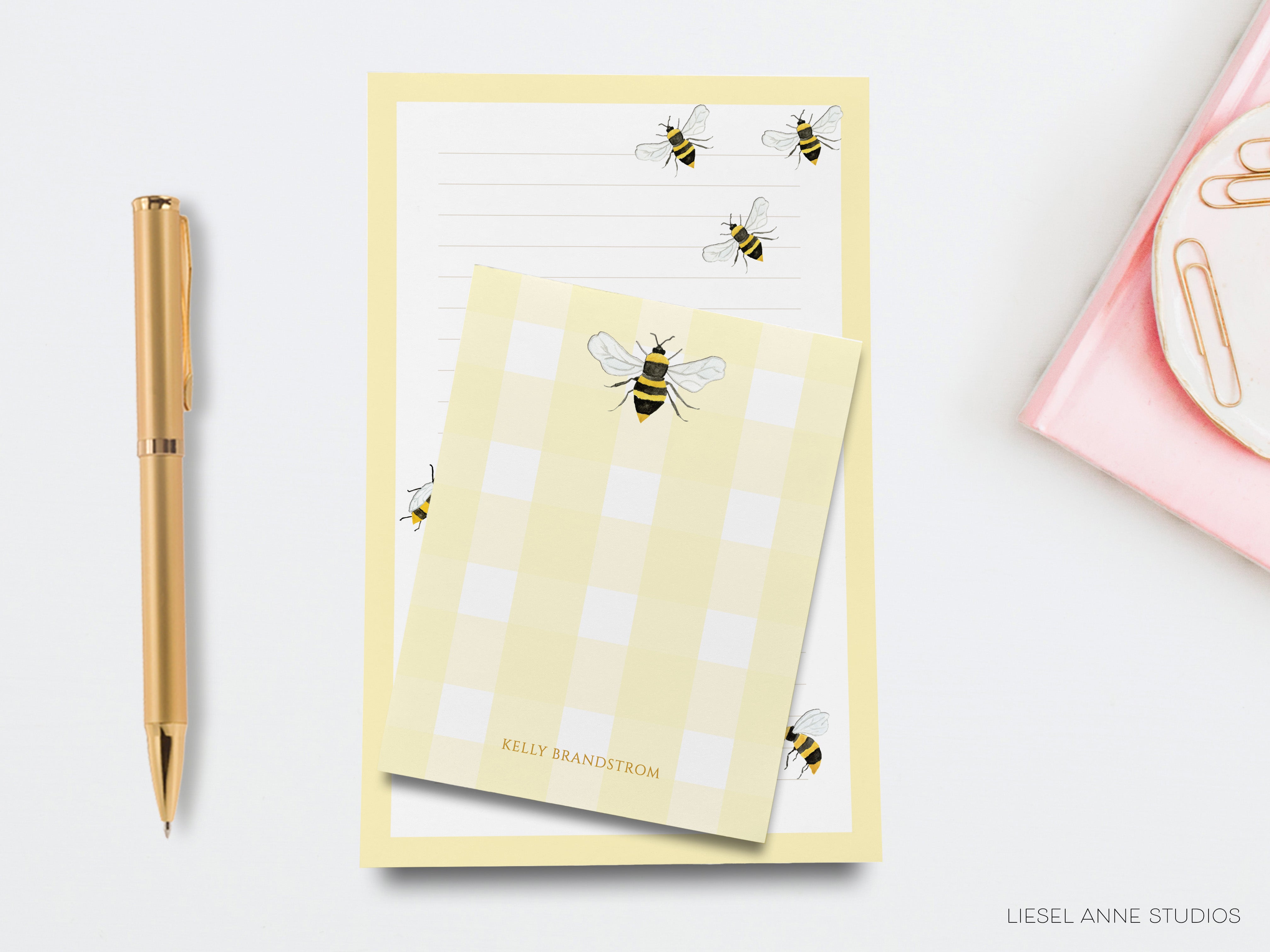 a yellow notepad with a checkered pattern, a gold pen, and a pink object, all placed on a white surface.