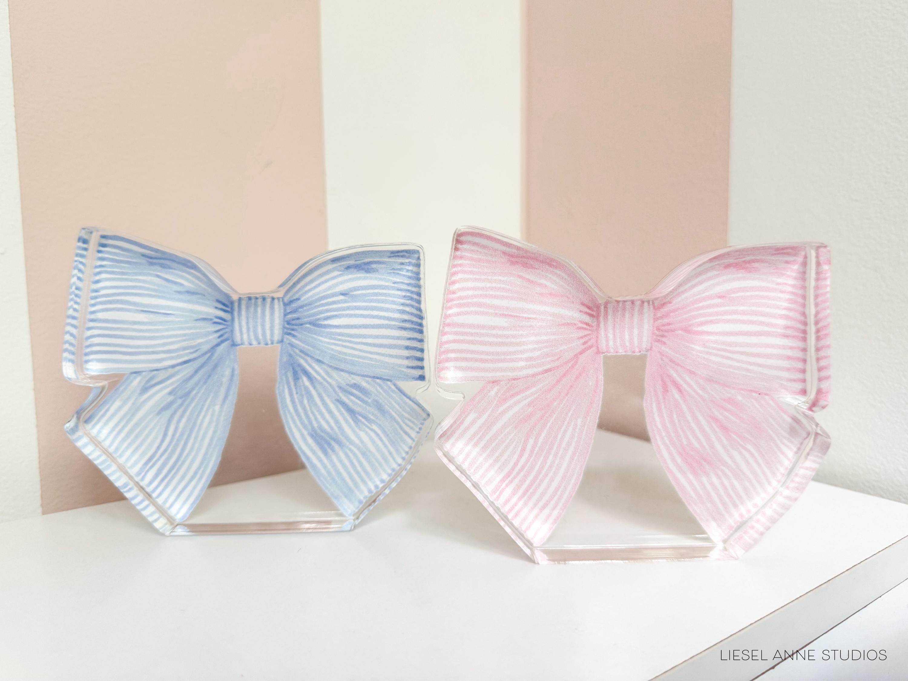 Two decorative bows in different colors - blue and pink - are displayed on a white surface.