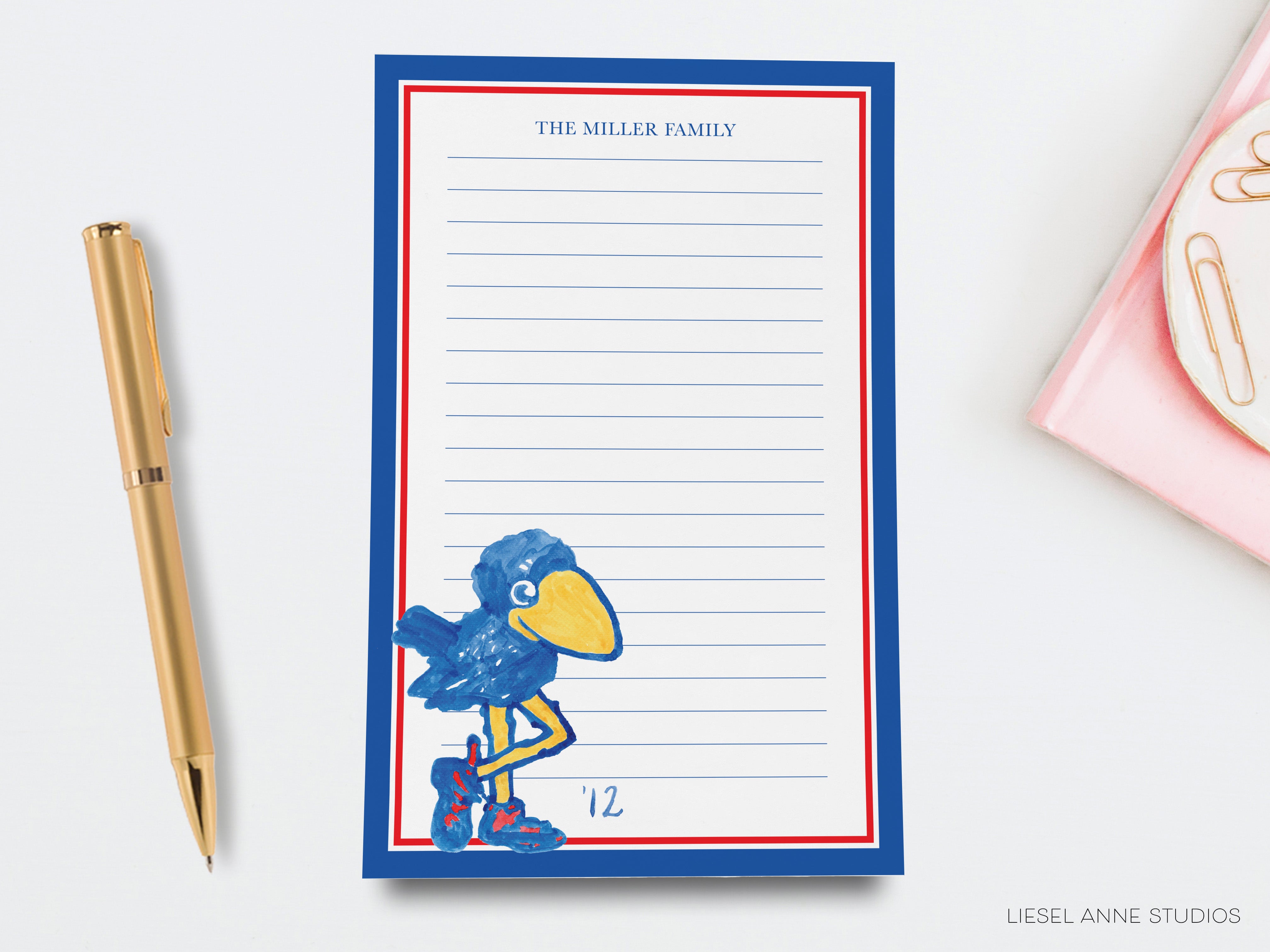 a blue and red lined paper pad with a drawing of a blue bird, accompanied by a gold pen and a pink object on a white background.