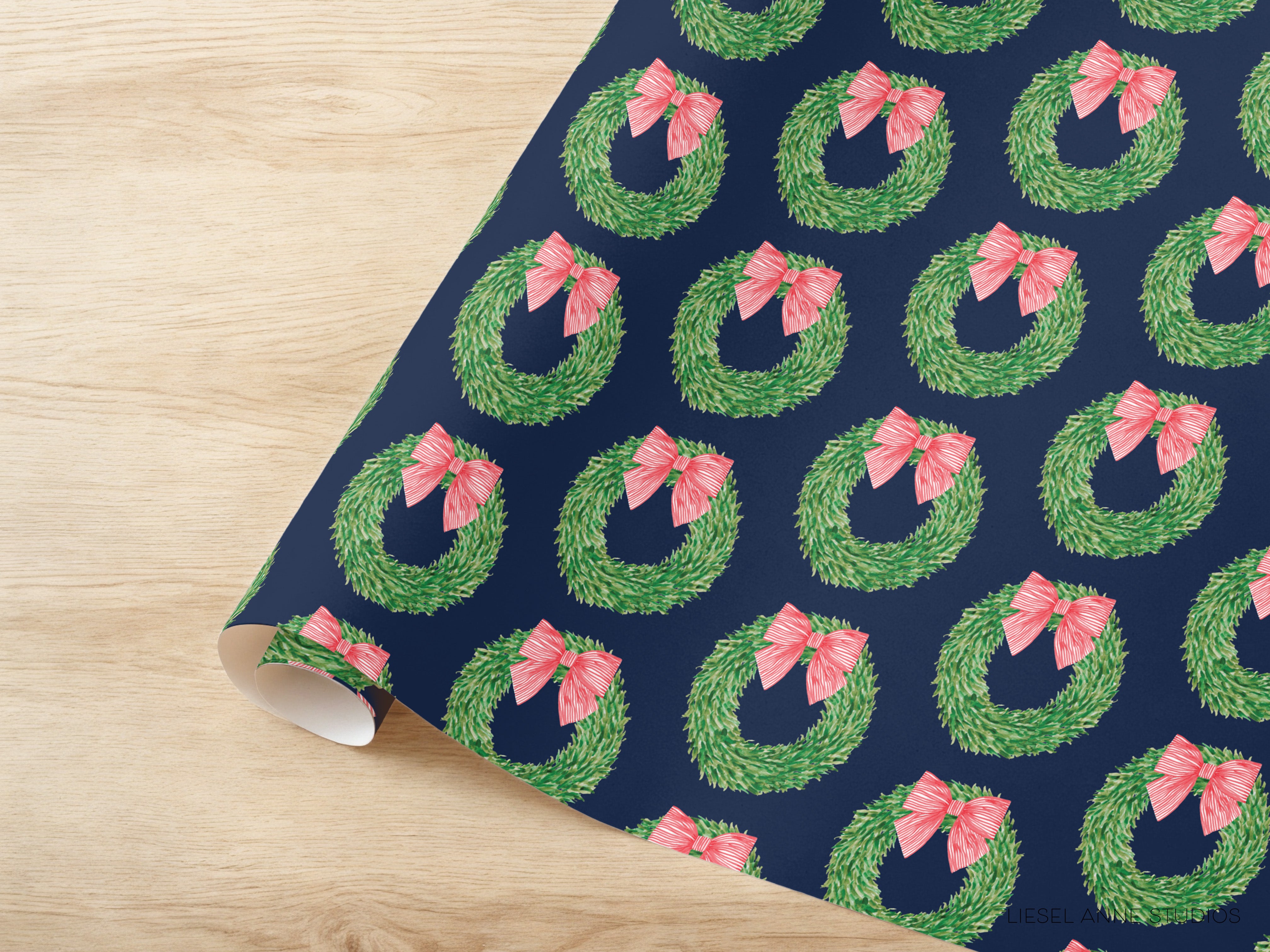 a roll of wrapping paper with a repeating pattern of green wreaths with pink bows on a dark blue background.