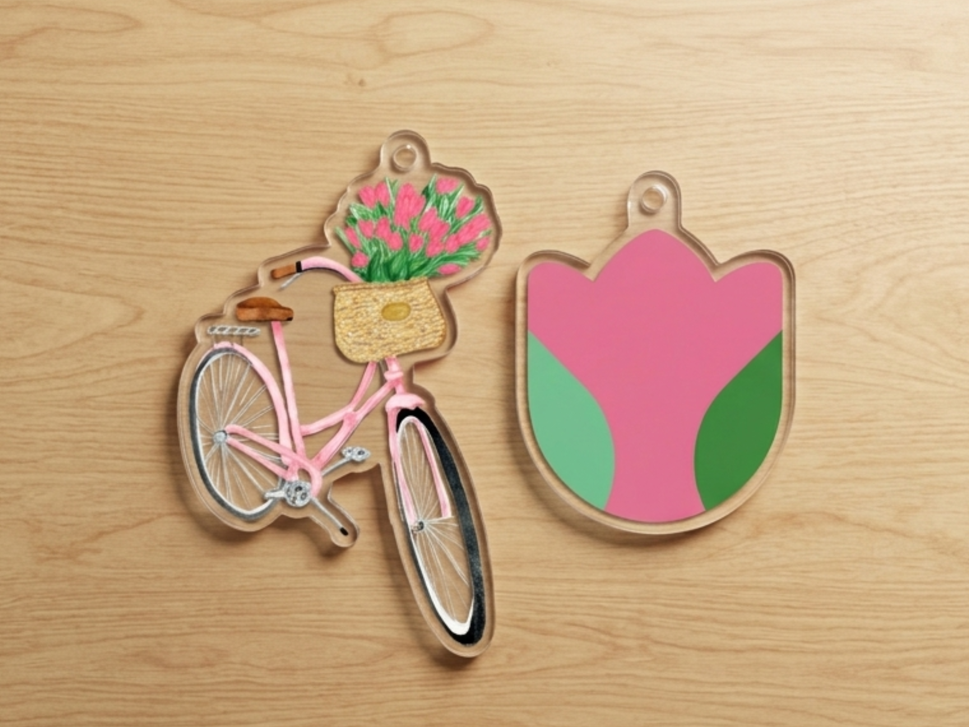 two clear plastic charms, one depicting a pink bicycle with a basket of pink flowers and the other depicting a pink flower-shaped charm.