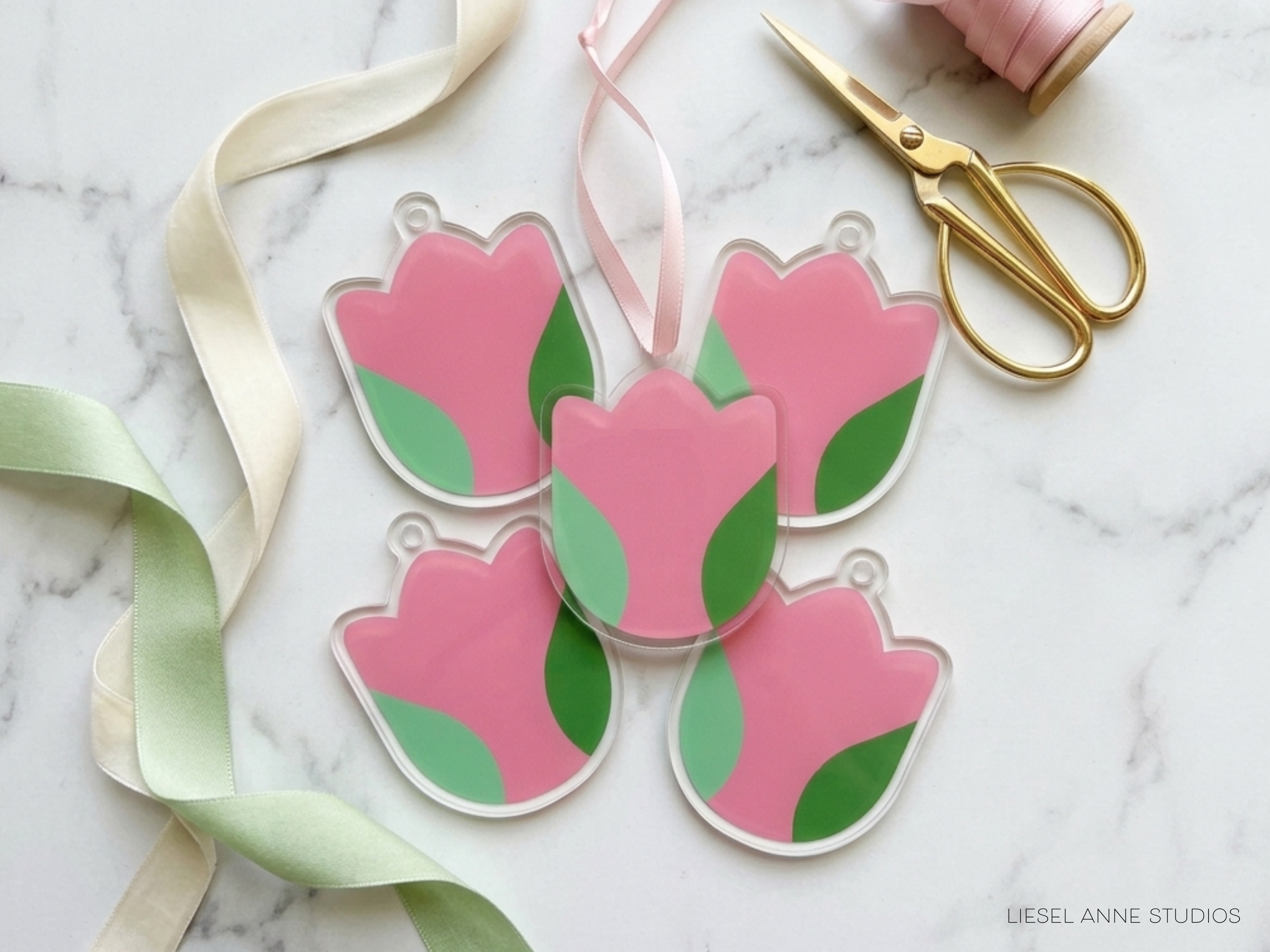 a collection of pink and green flower-shaped ornaments, along with a pair of scissors and a ribbon, all arranged on a marble surface.