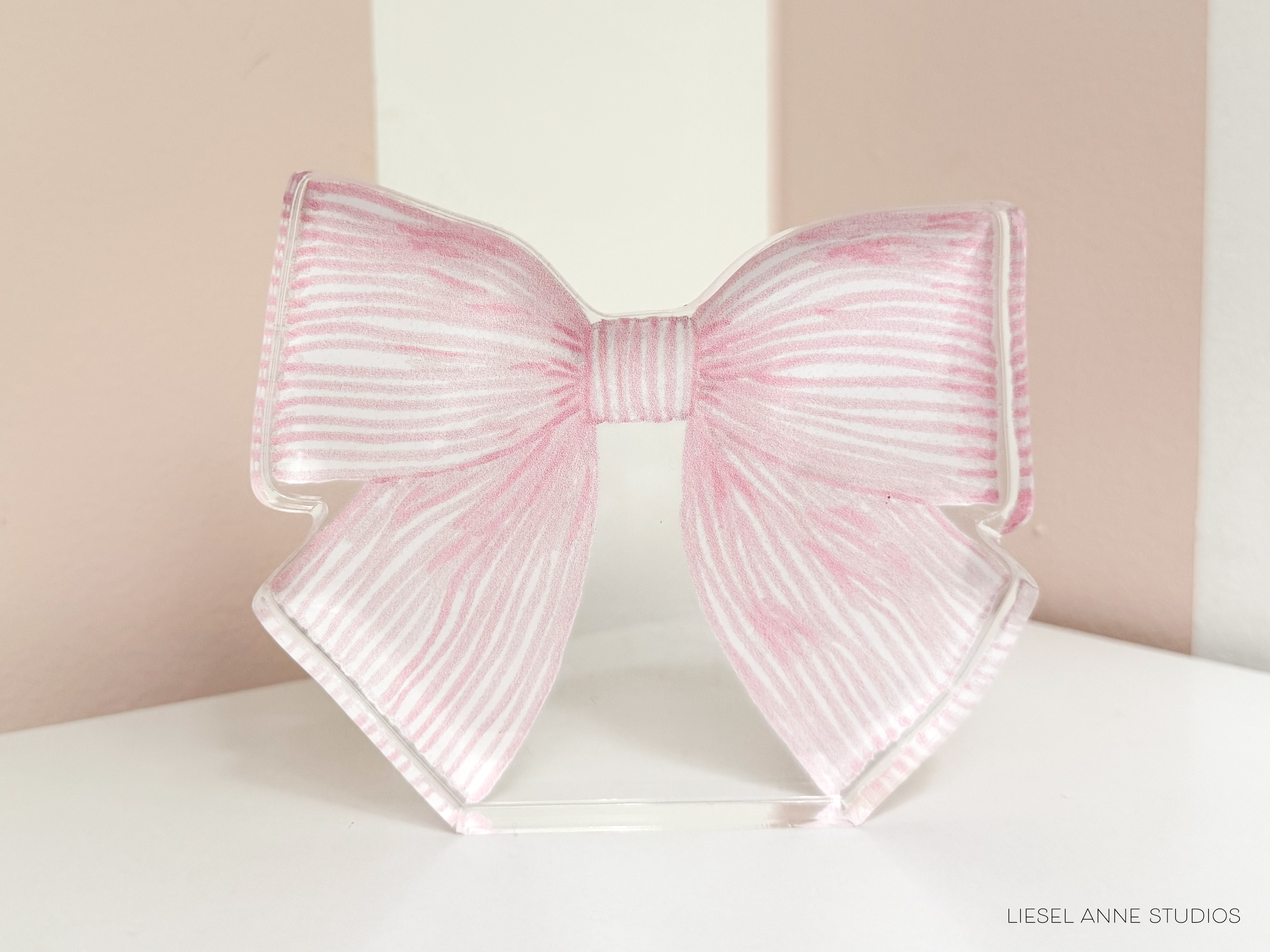 A pink and white striped bow tie is displayed on a white surface against a pink and white striped background.