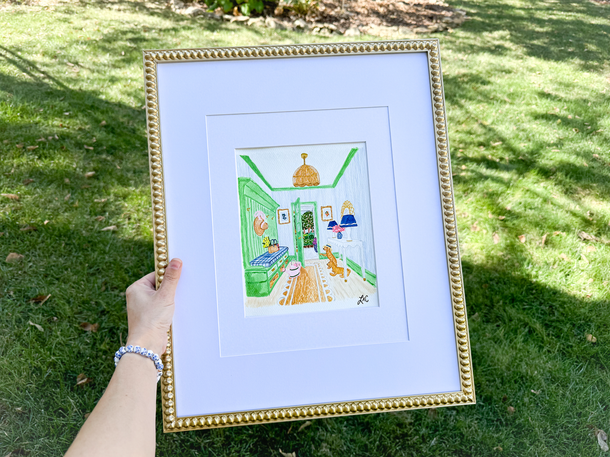 A hand holding a framed painting of a colorful interior scene, with a green and white color scheme and various objects and furniture.
