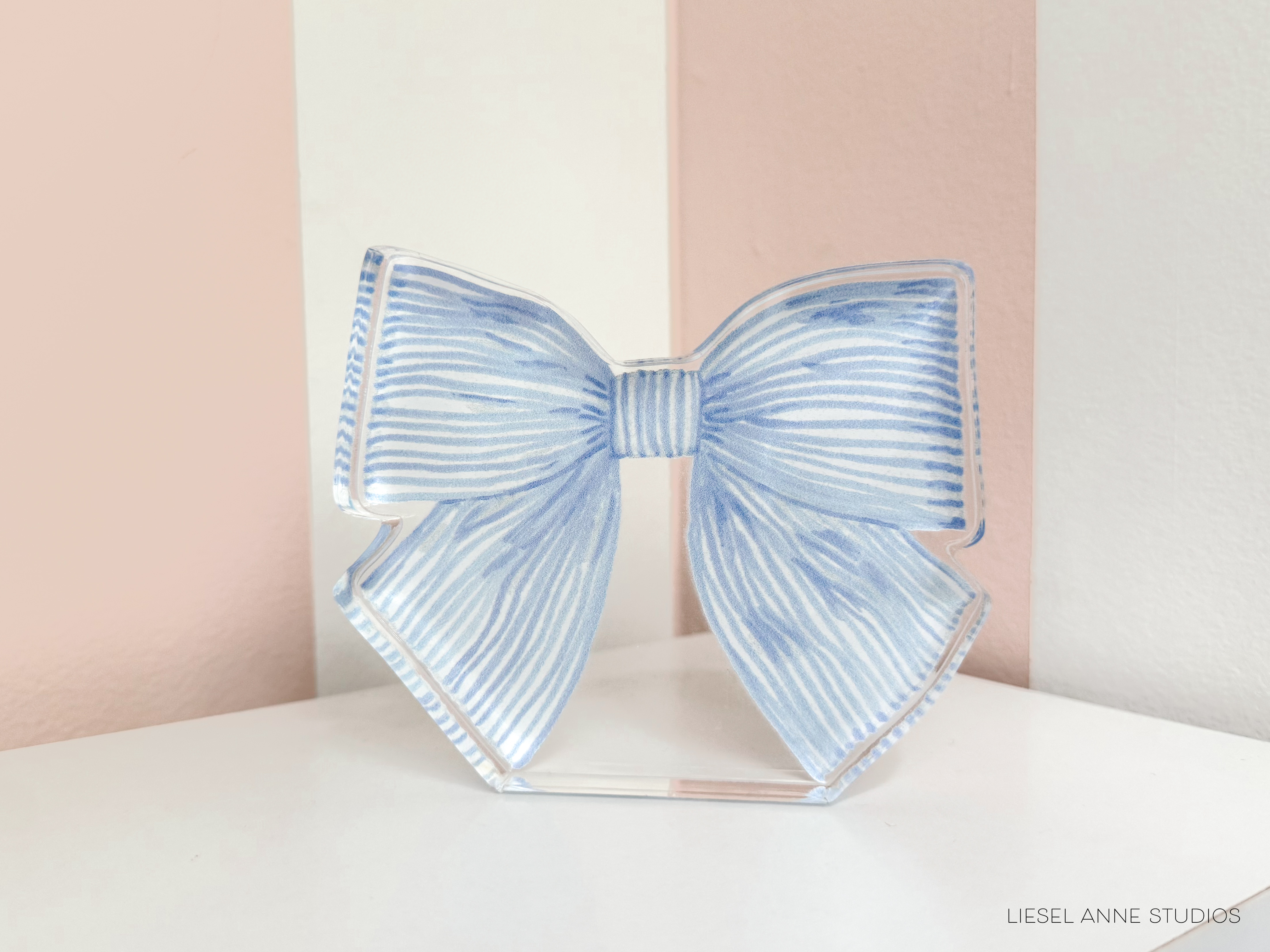 A blue and white striped bow tie is displayed on a white surface against a pink and white striped background.