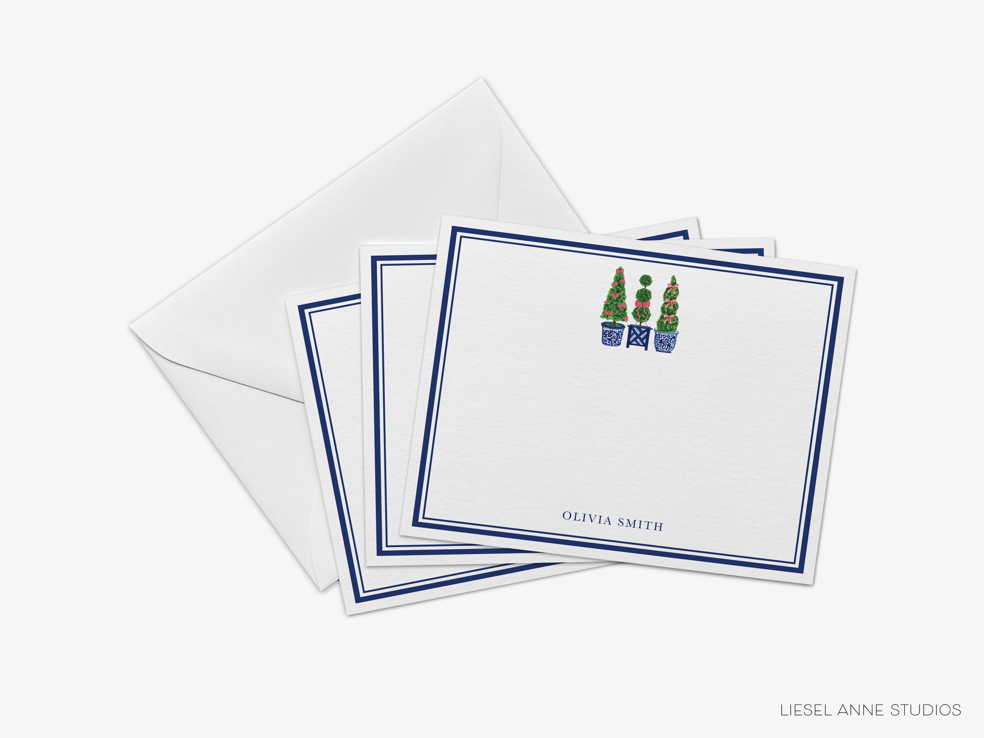 a set of white greeting cards with blue borders, each featuring a small illustration of a Christmas tree. The cards are neatly arranged in a stack, with the top card slightly overlapping the others. The text "OLIVIA SMITH" is visible on the bottom card, indicating the name of the sender.
