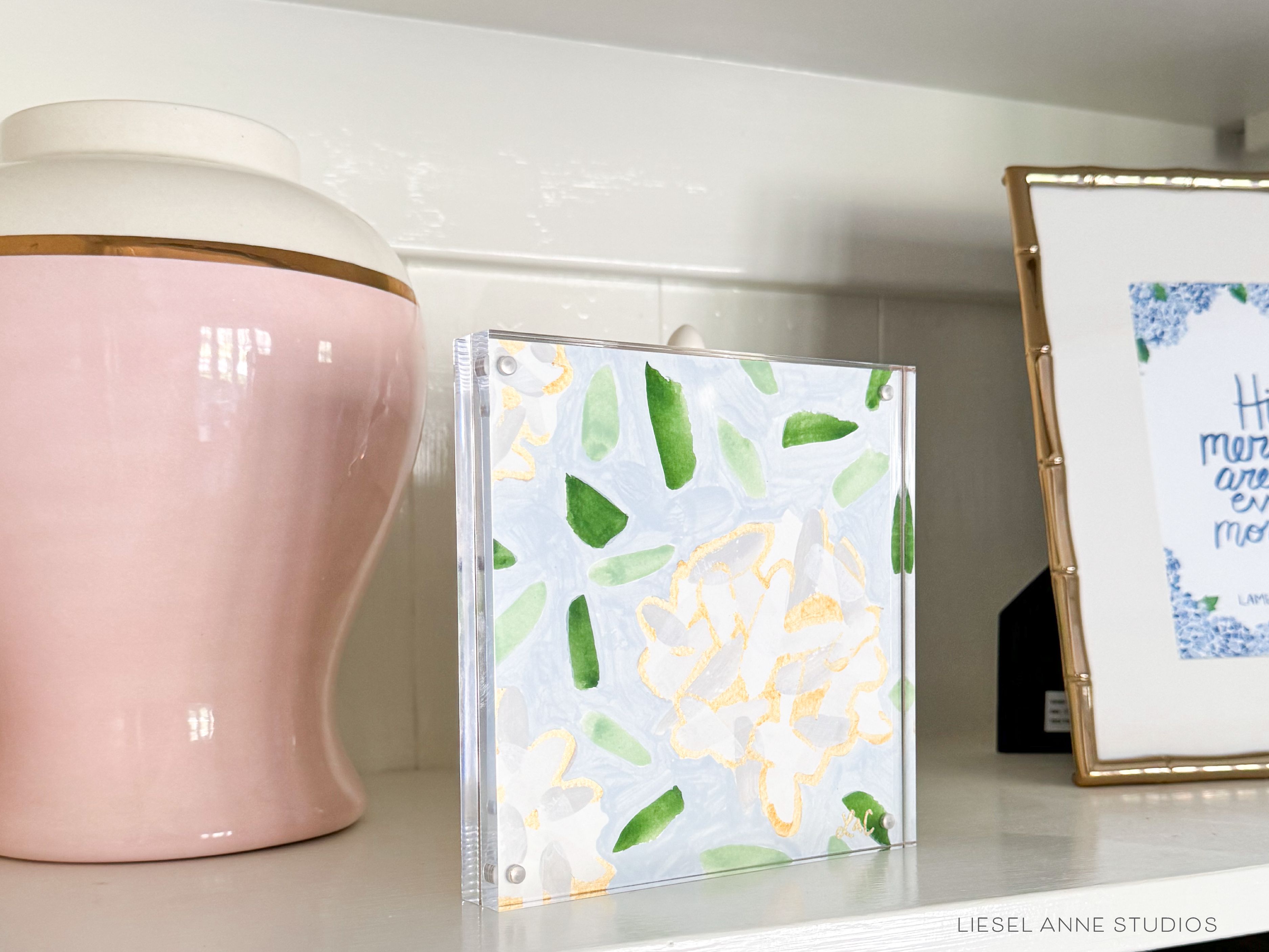 Golden Hydrangea Mini | Blue & White 01-Original artwork measures 6"x6" | Hand-Painted with gouache on cold press watercolor paper | Framed in clear acrylic magnetic block frame | Features our signature Golden Hydrangea design with a light blue base, white hydrangeas and shimmery gold accents | Initialed in gold by the Liesel Anne (the artist) on the front and signed and dated on the back-The Singing Little Bird