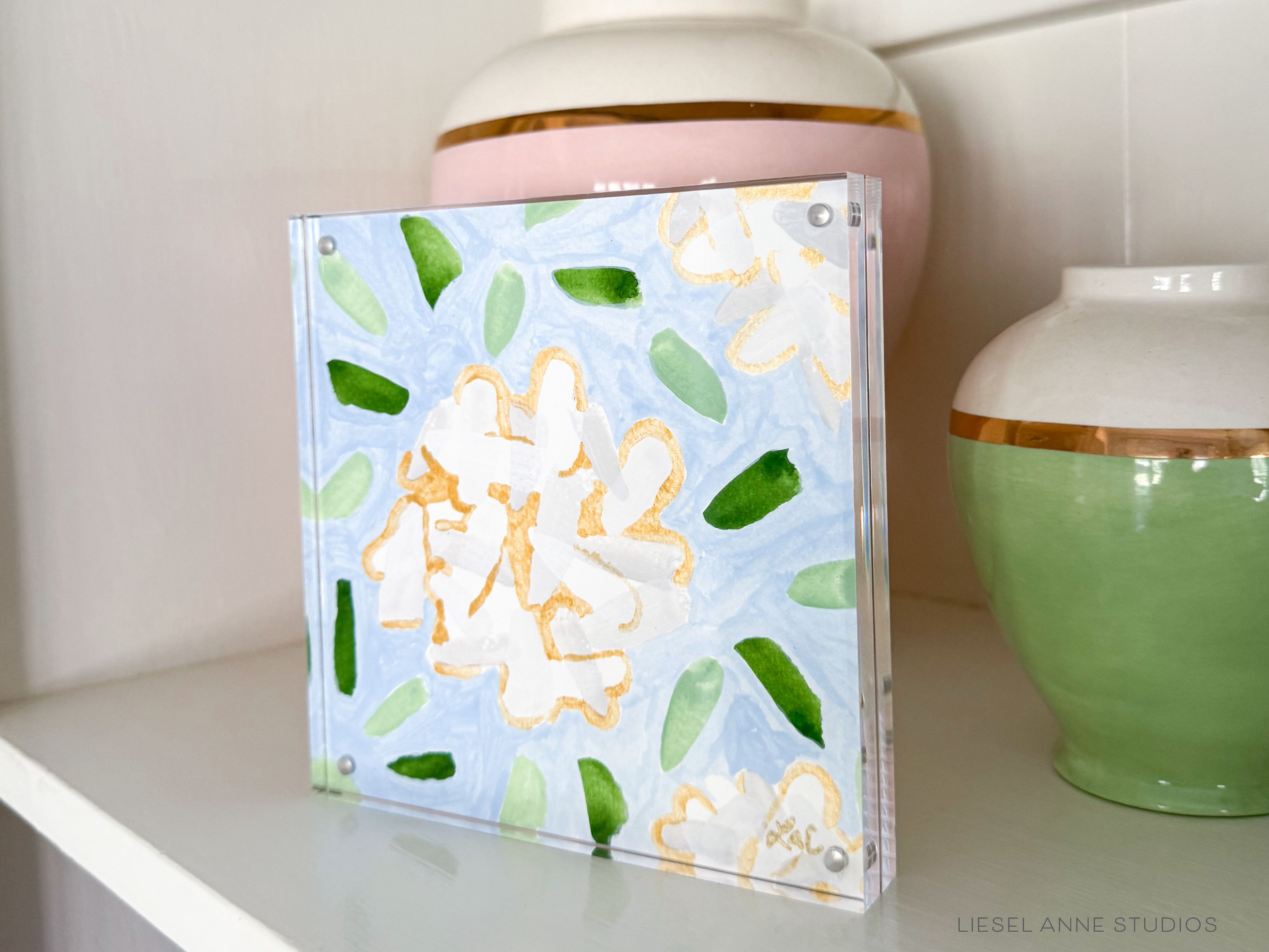 Golden Hydrangea Mini | Blue & White 05-Original artwork measures 6"x6" | Hand-Painted with gouache on cold press watercolor paper | Framed in clear acrylic magnetic block frame | Features our signature Golden Hydrangea design with a light blue base, white hydrangeas and shimmery gold accents | Initialed in gold by the Liesel Anne (the artist) on the front and signed and dated on the back-The Singing Little Bird