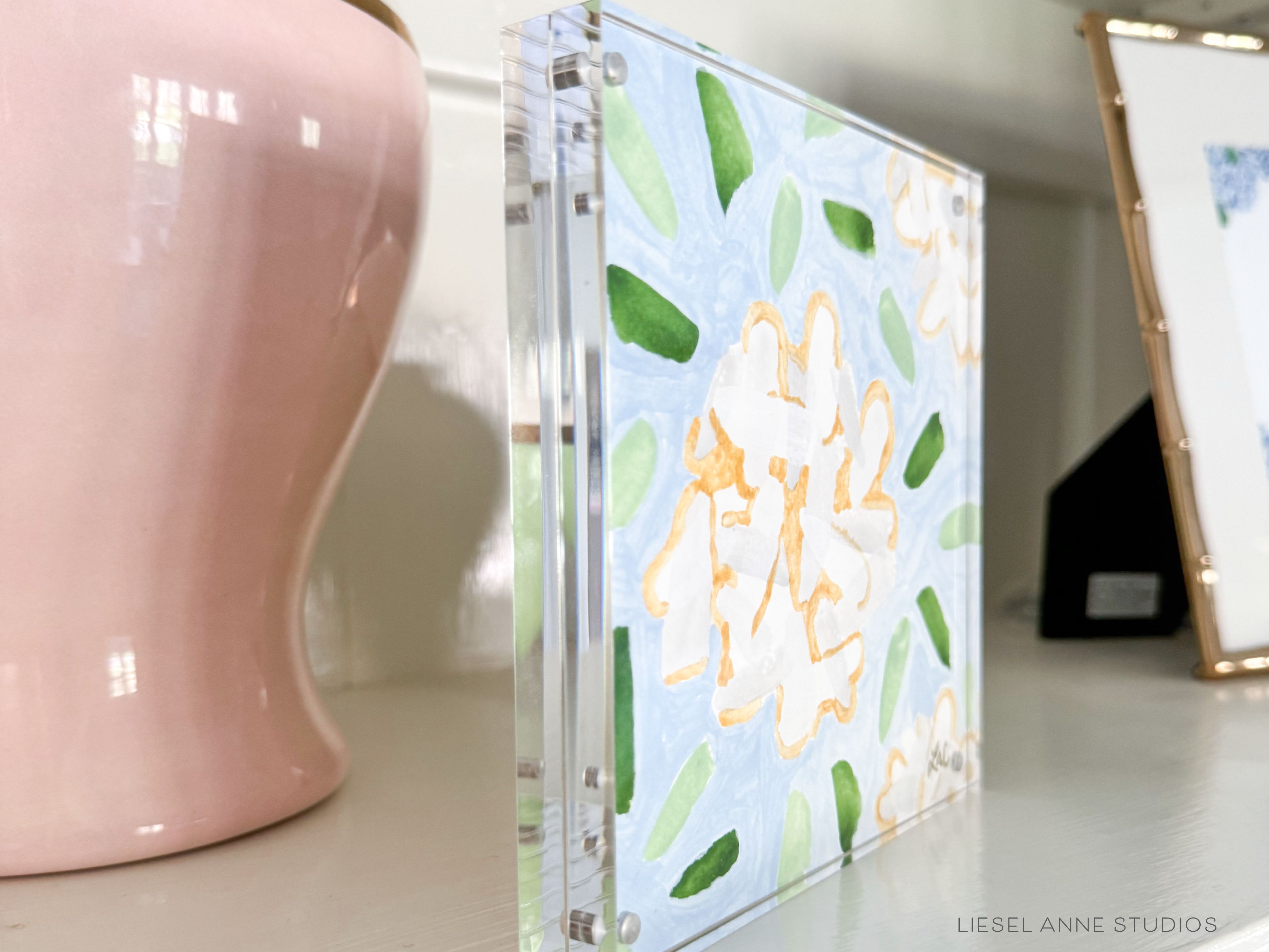 Golden Hydrangea Mini | Blue & White 05-Original artwork measures 6"x6" | Hand-Painted with gouache on cold press watercolor paper | Framed in clear acrylic magnetic block frame | Features our signature Golden Hydrangea design with a light blue base, white hydrangeas and shimmery gold accents | Initialed in gold by the Liesel Anne (the artist) on the front and signed and dated on the back-The Singing Little Bird