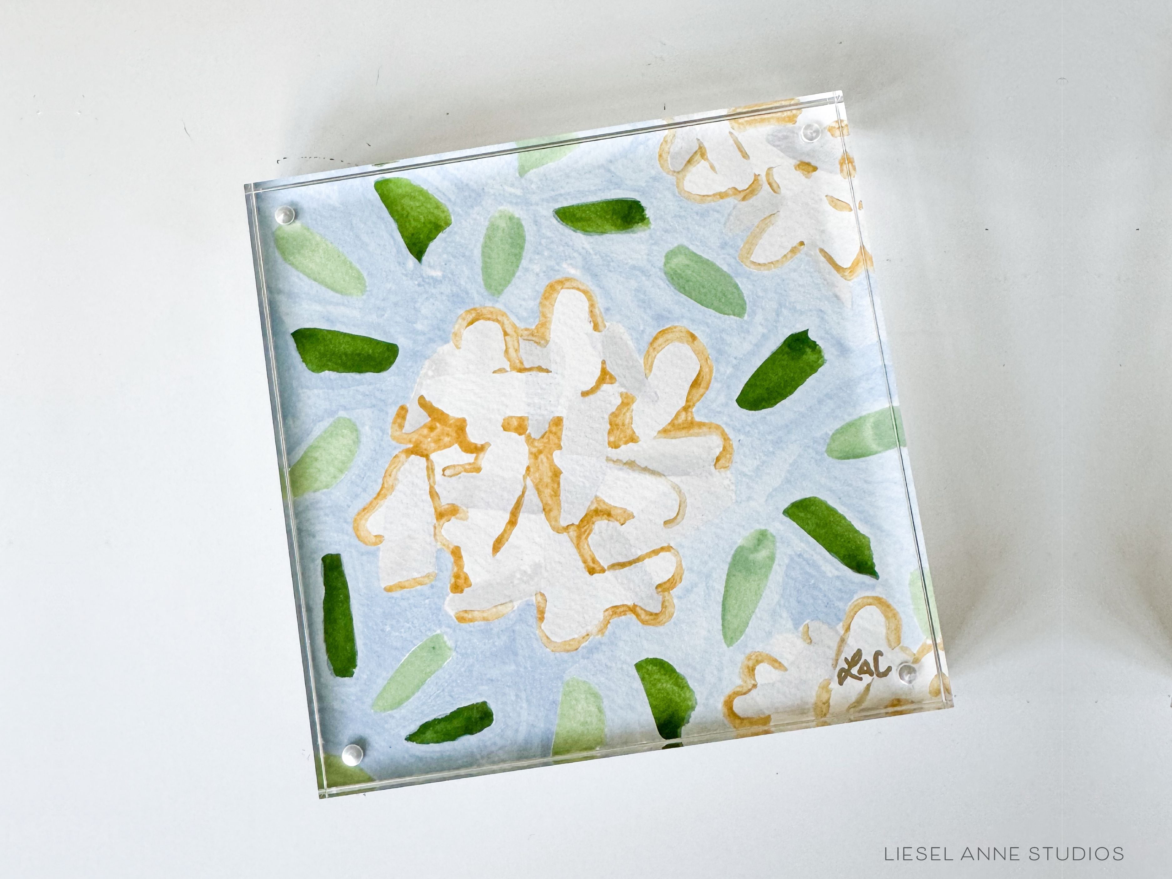 Golden Hydrangea Mini | Blue & White 05-Original artwork measures 6"x6" | Hand-Painted with gouache on cold press watercolor paper | Framed in clear acrylic magnetic block frame | Features our signature Golden Hydrangea design with a light blue base, white hydrangeas and shimmery gold accents | Initialed in gold by the Liesel Anne (the artist) on the front and signed and dated on the back-The Singing Little Bird