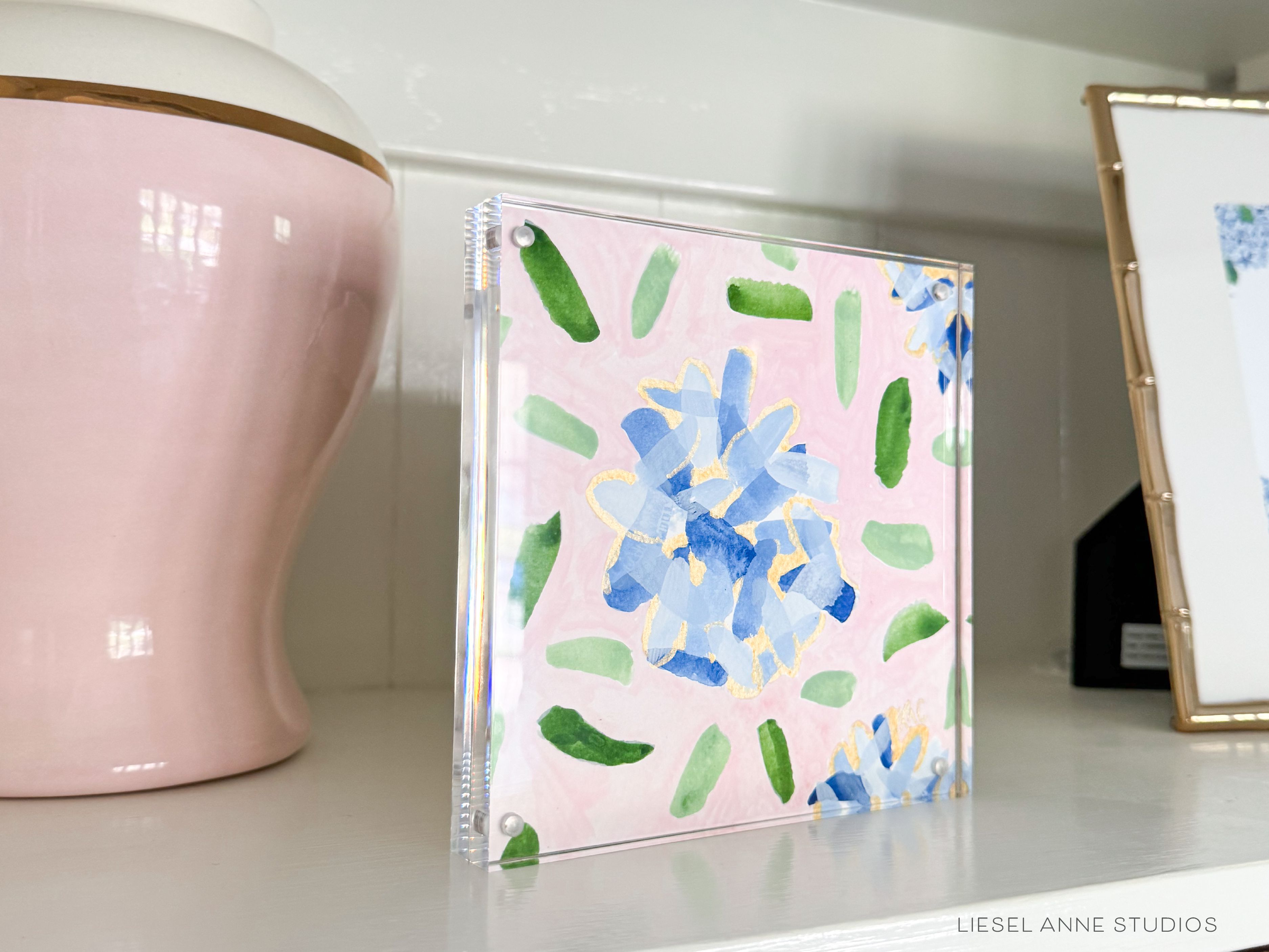 Golden Hydrangea Mini | Pink & Blue 03-Original artwork measures 6"x6" | Hand-Painted with gouache on cold press watercolor paper | Framed in clear acrylic magnetic block frame | Features our signature Golden Hydrangea design with a pale pink base, blue hydrangeas and shimmery gold accents | Initialed in gold by the Liesel Anne (the artist) on the front and signed and dated on the back-The Singing Little Bird