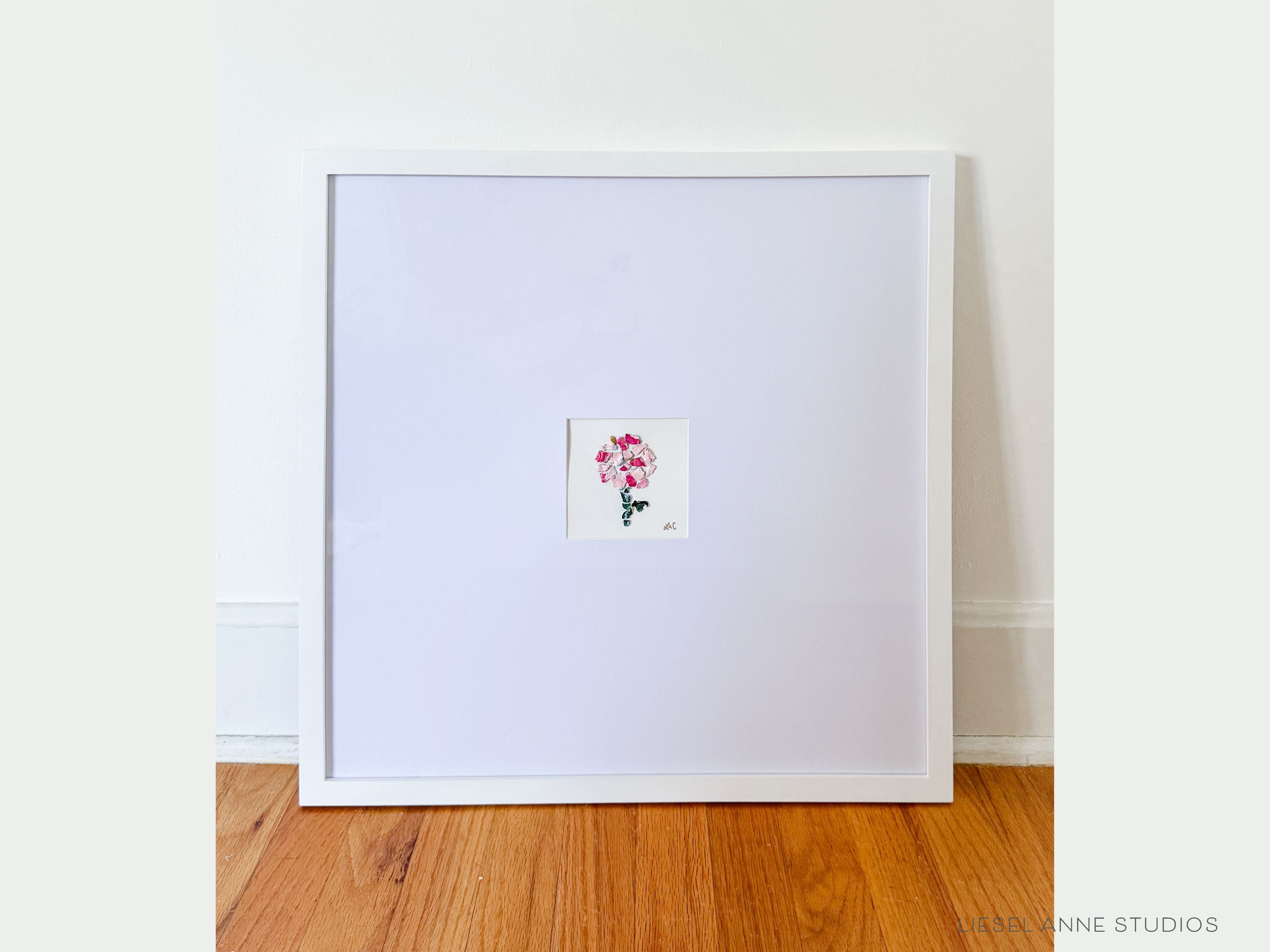 Golden Hydrangea | Paint Chip | Multi-Pink on White XIV-Original artwork measures 4" x 4"| Matted and framed in white wood frame sized 20" x 20" | Base Hand-Painted with gouache on cold press watercolor paper | Acrylic Paint Chip Pieces hand-torn from pain pallet and placed in "mosaic" form, secured to the base | UV shielding acrylic glass | Hanging hardware included | Features our signature Golden Hydrangea design with a pale pink base, blue hydrangeas and shimmery gold accents | Initialed in gold by Liese