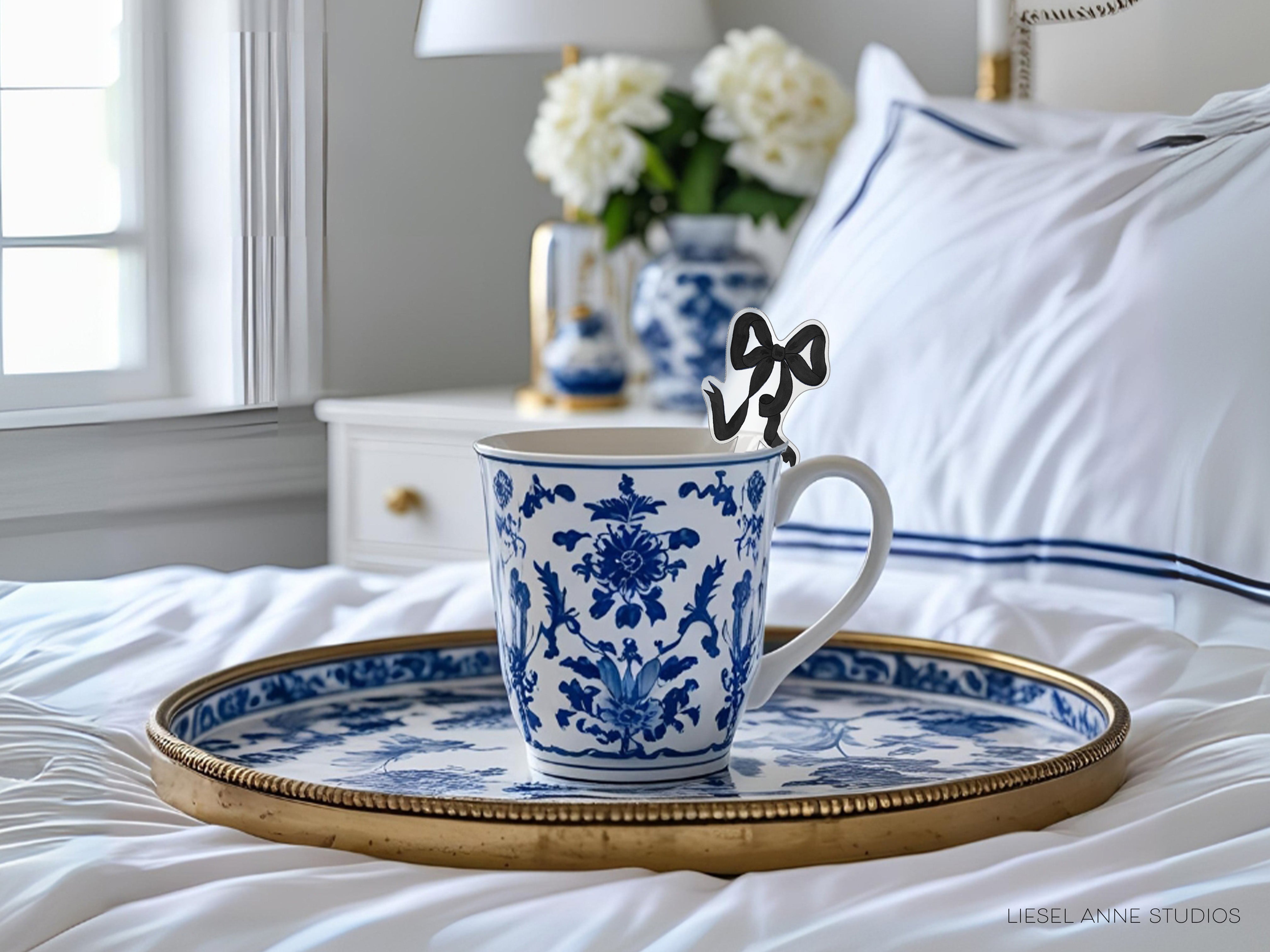 A blue and white patterned mug sits on a gold tray, with a vase of white flowers in the background.