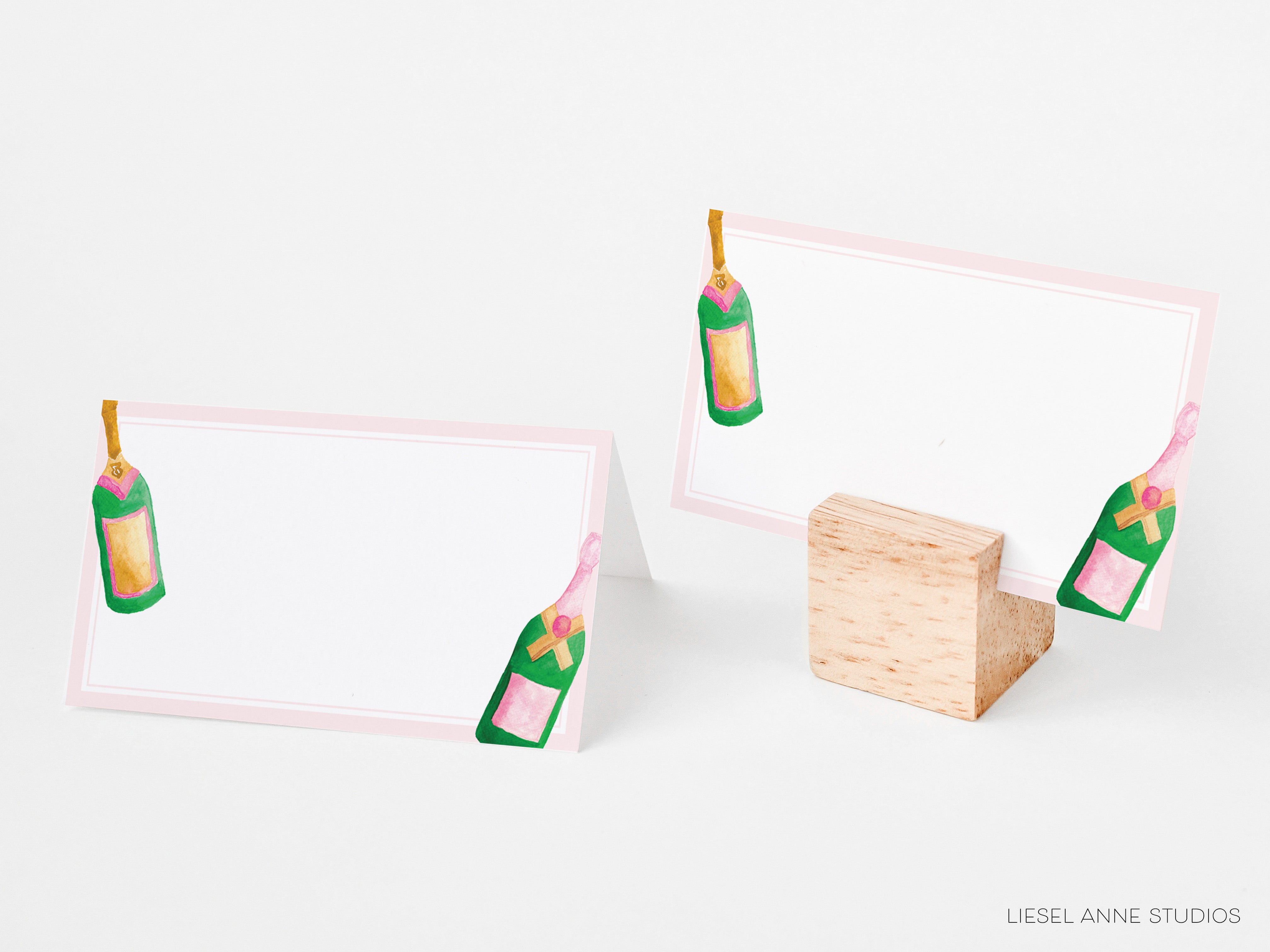 two blank place cards with champagne bottle illustrations on them, placed on a wooden stand.