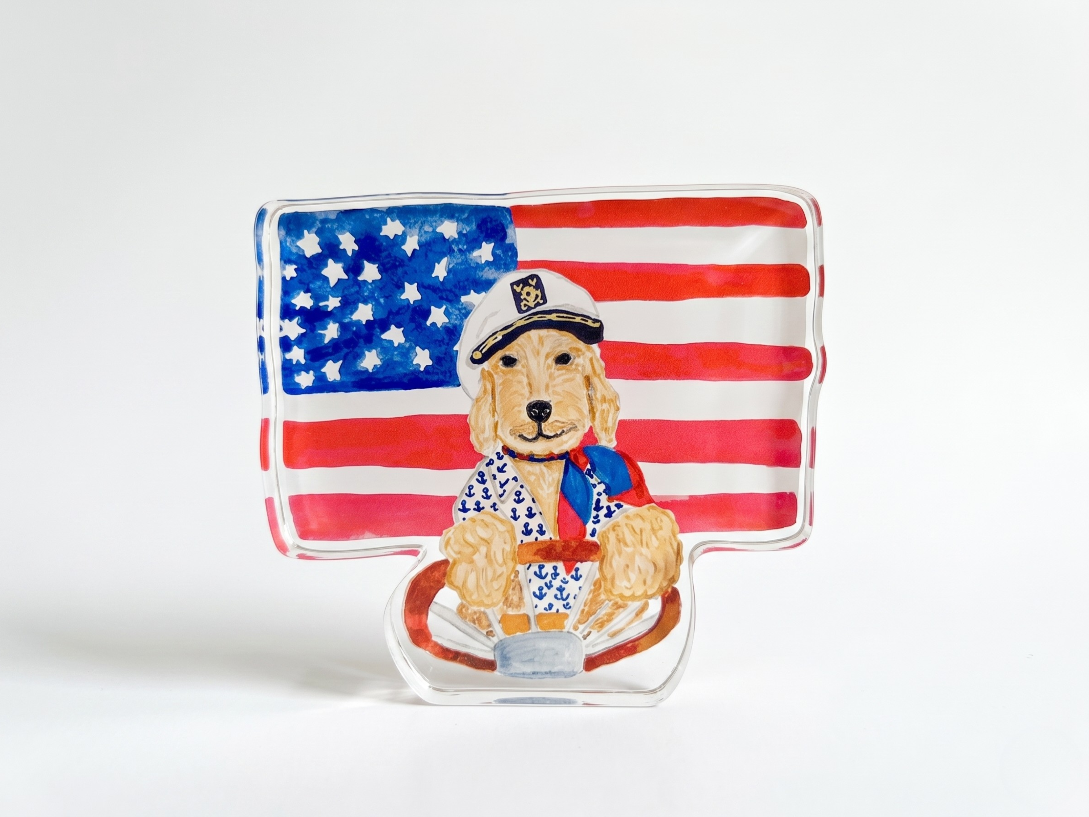 A glass sculpture depicting a dog wearing a sailor's hat and a sailor's outfit, with an American flag in the background.