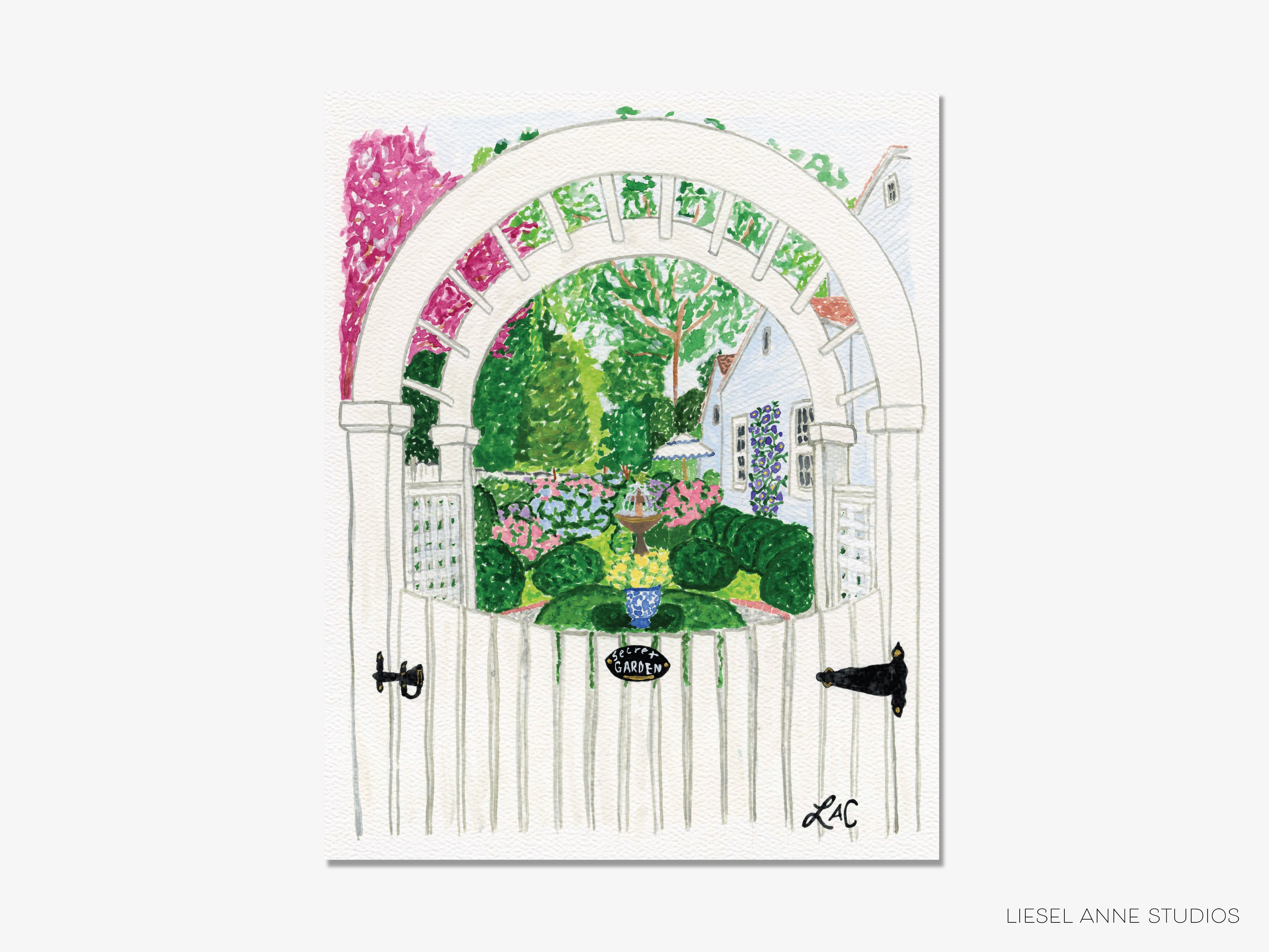 A white wooden gate with a decorative archway, surrounded by a lush garden with colorful flowers and greenery.