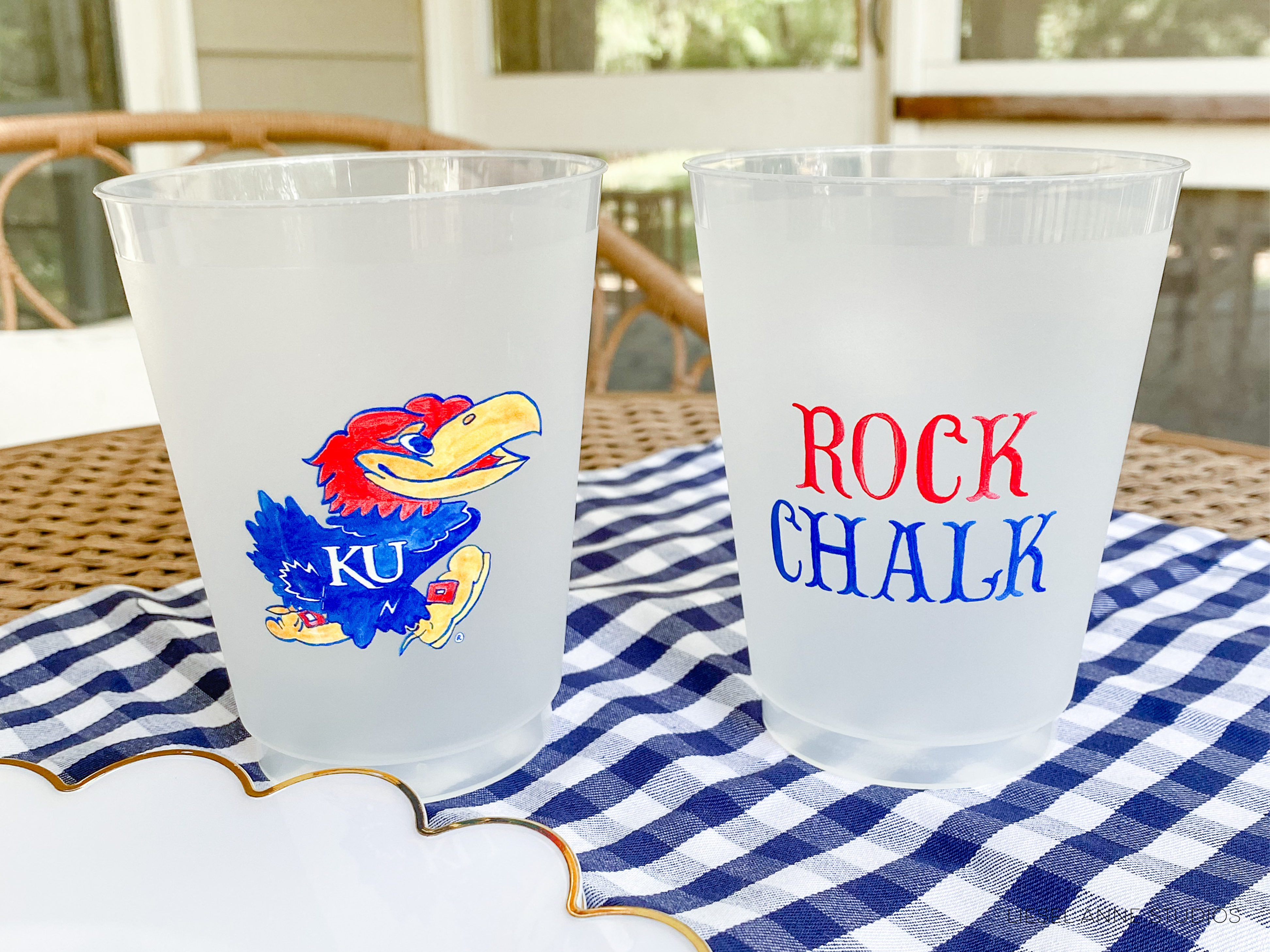 Two clear plastic cups with the text "ROCK CHALK" printed on them, placed on a blue and white checkered tablecloth.