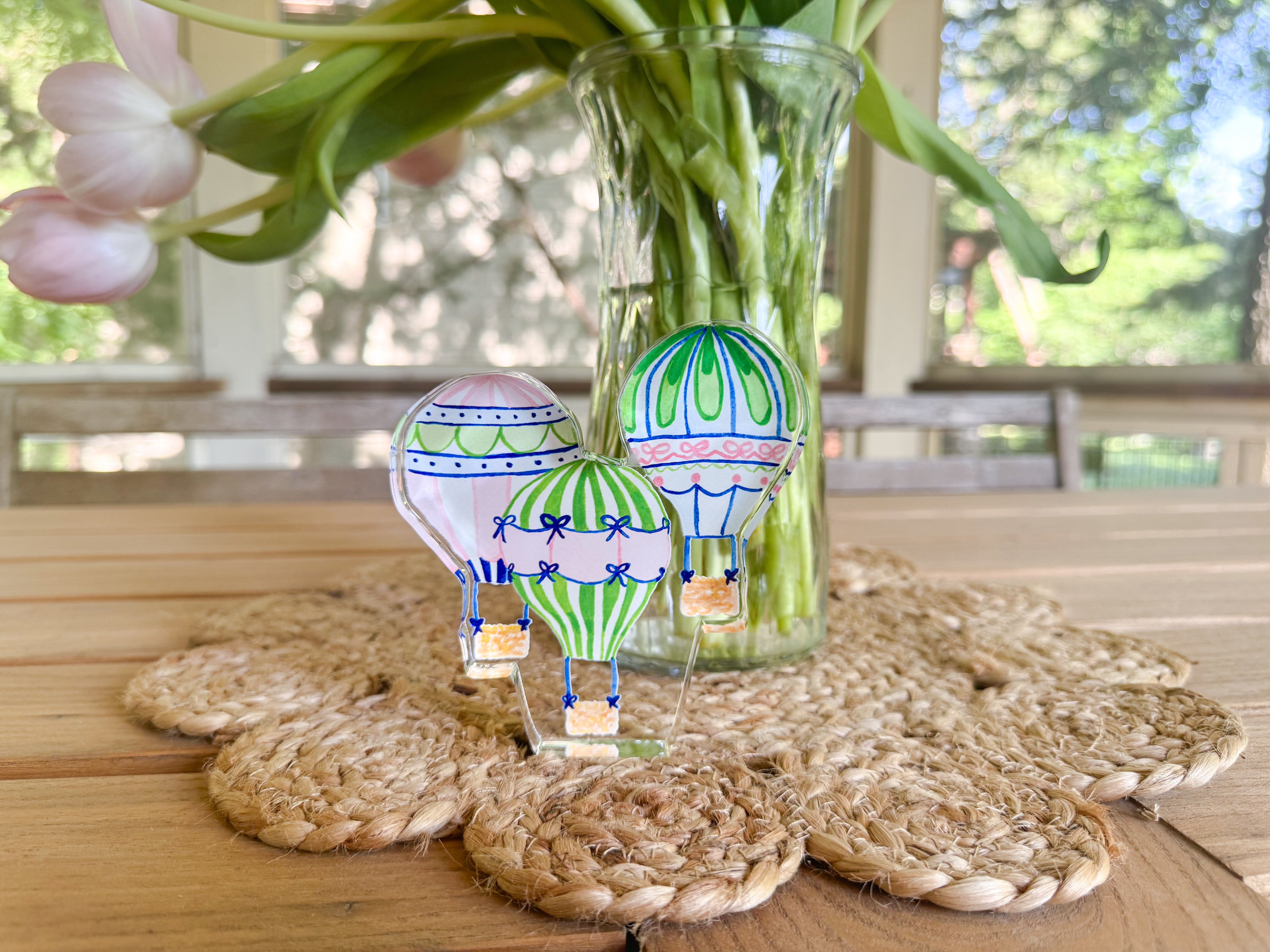 a table with a vase of flowers, a woven placemat, and three glass figurines shaped like hot air balloons.