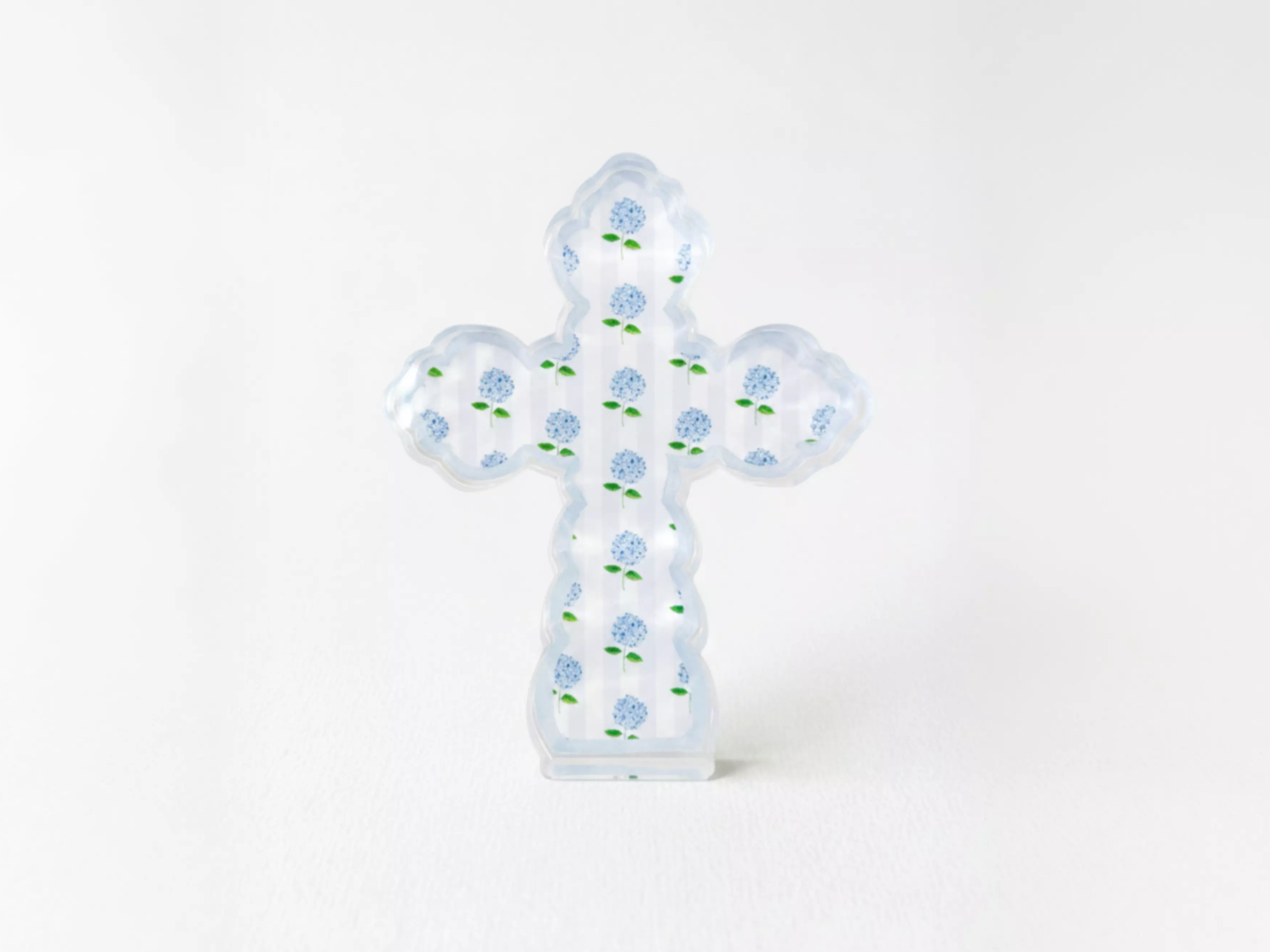 A clear glass cross with blue flowers on it, standing upright against a white background.