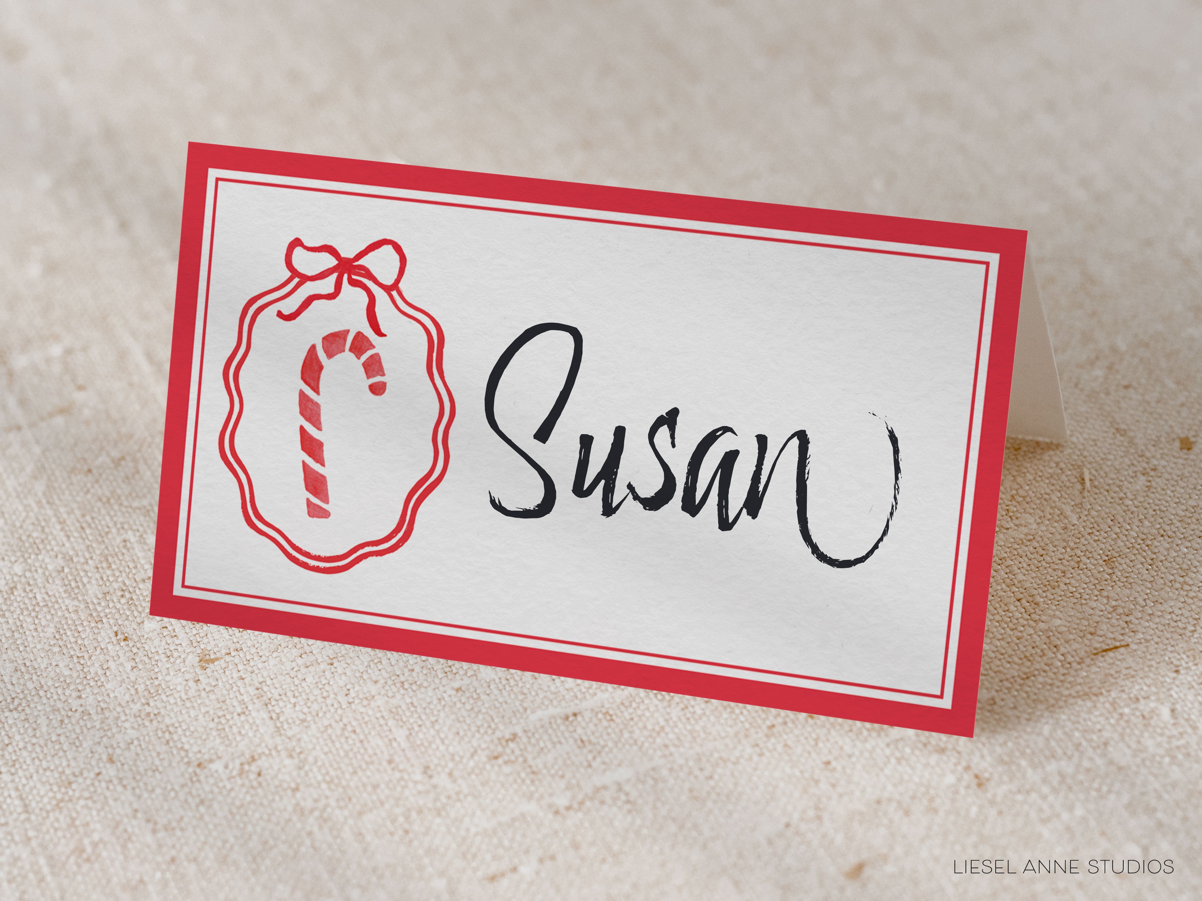 A white name card with a red border, featuring a red ribbon and a candy cane icon, and the name "Susan" written in black cursive text.