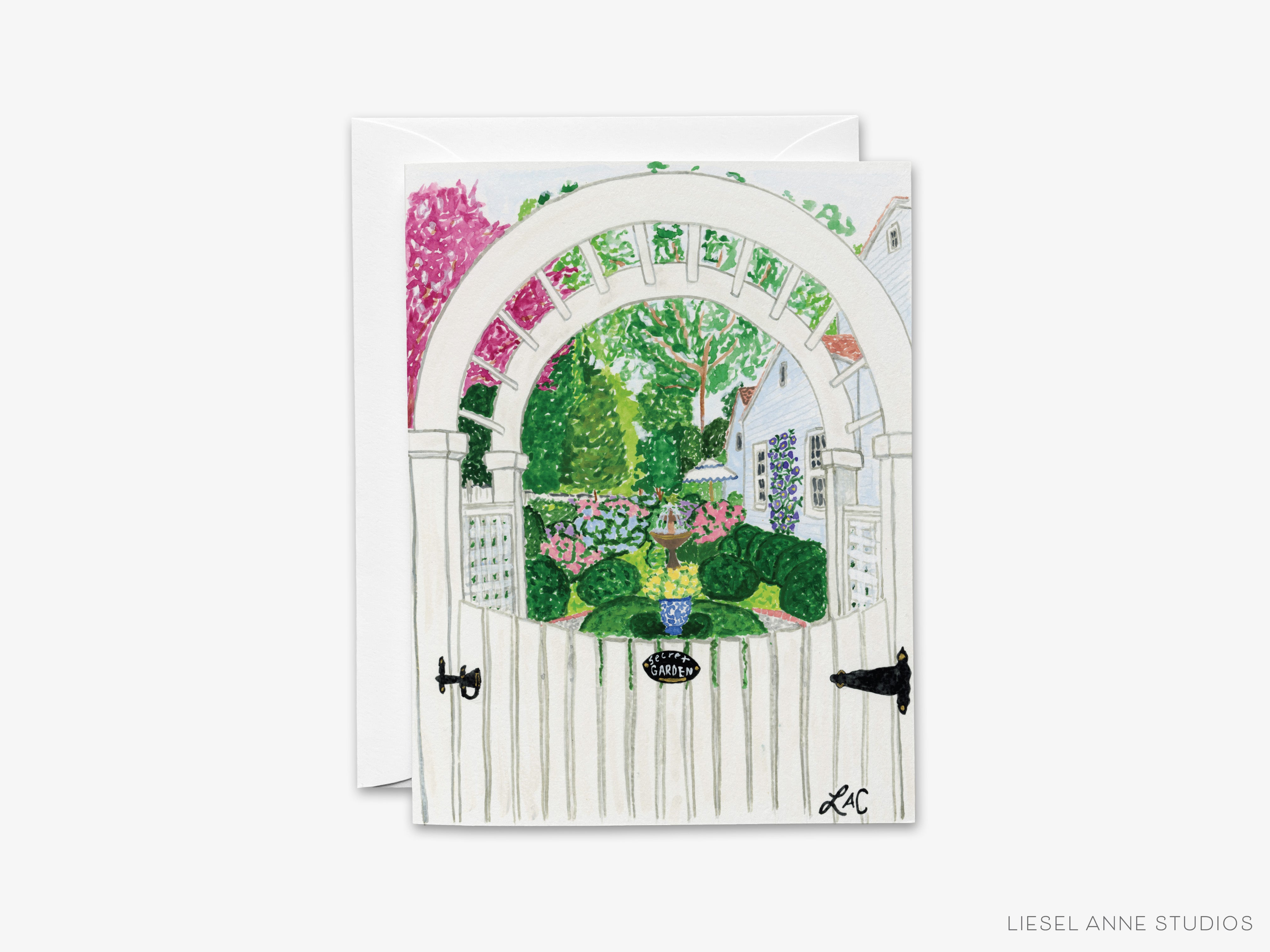 A white wooden gate with a decorative archway, surrounded by a lush garden with colorful flowers and greenery.
