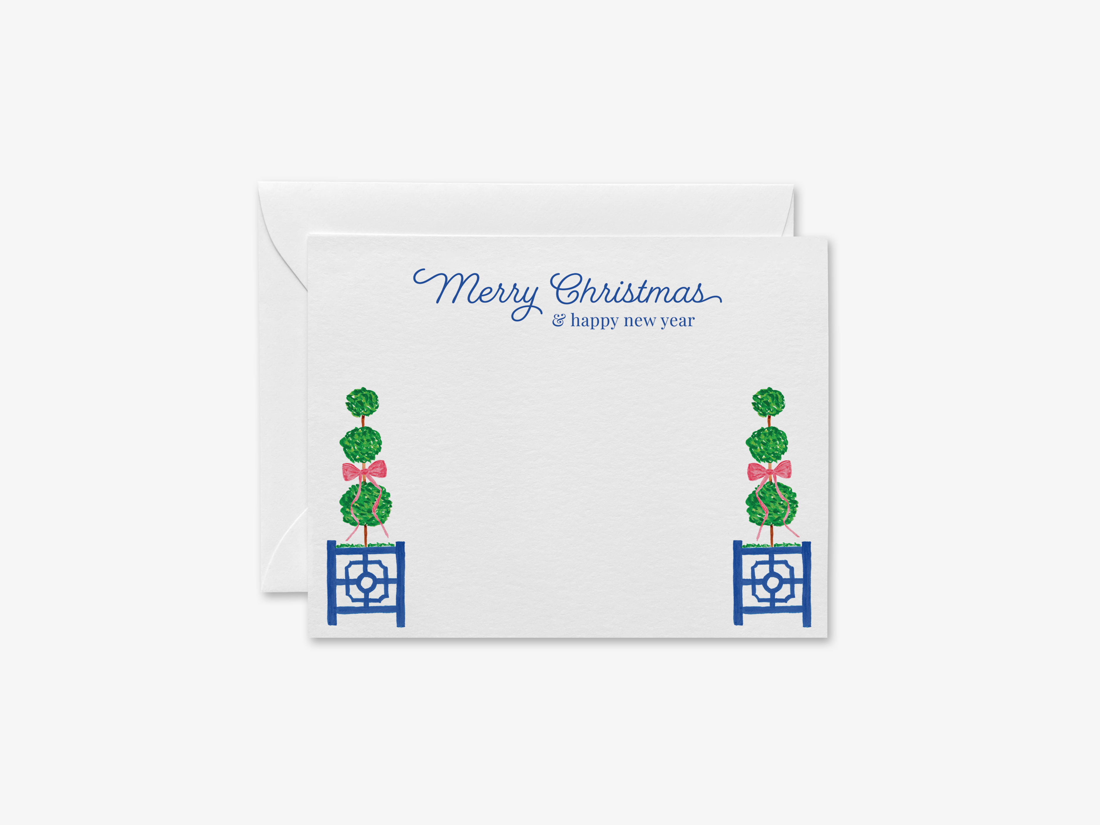 A white greeting card with a holiday message and decorative elements, including two green topiary trees with bows on either side of the card.