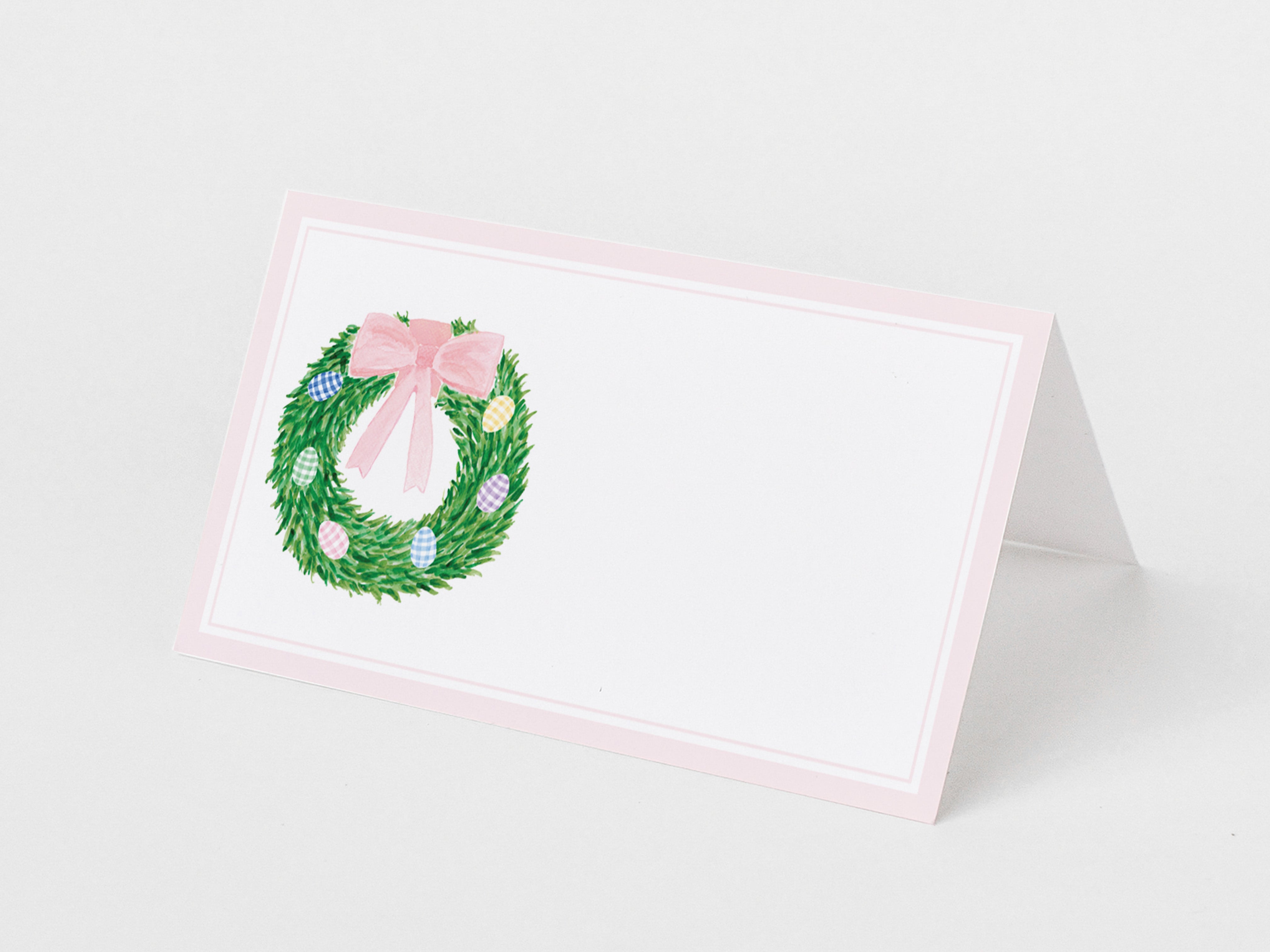 A pink and white card with a wreath and a pink ribbon on it.